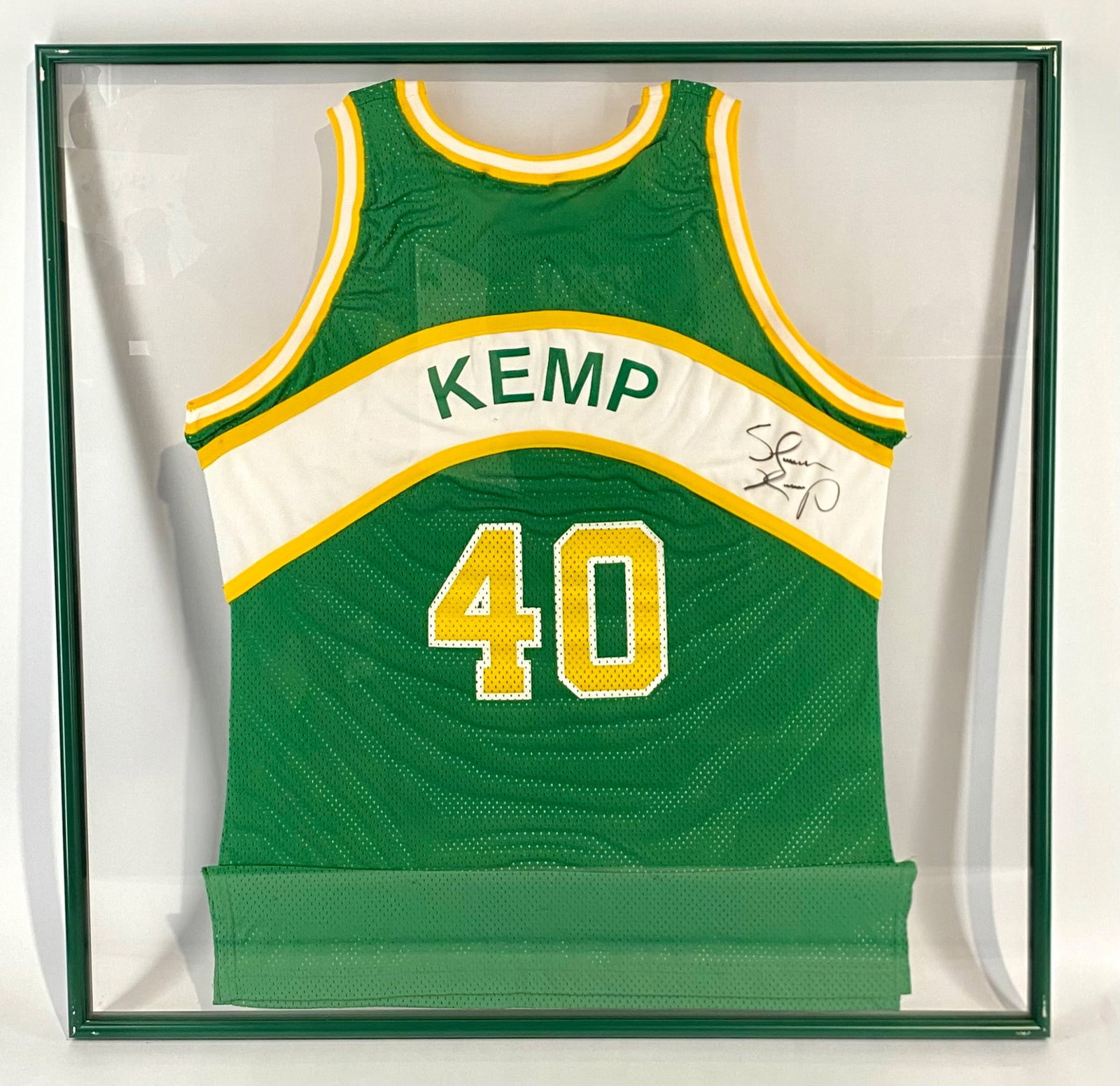 Seattle Supersonics Signed Shawn Kemp Jersey in Green Frame: Seattle Supersonics basketball jersey featuring player number 40 and name "Kemp." Manufactured by Champion, size 48, with official team and brand labels attached. Autographed on the upper right chest 