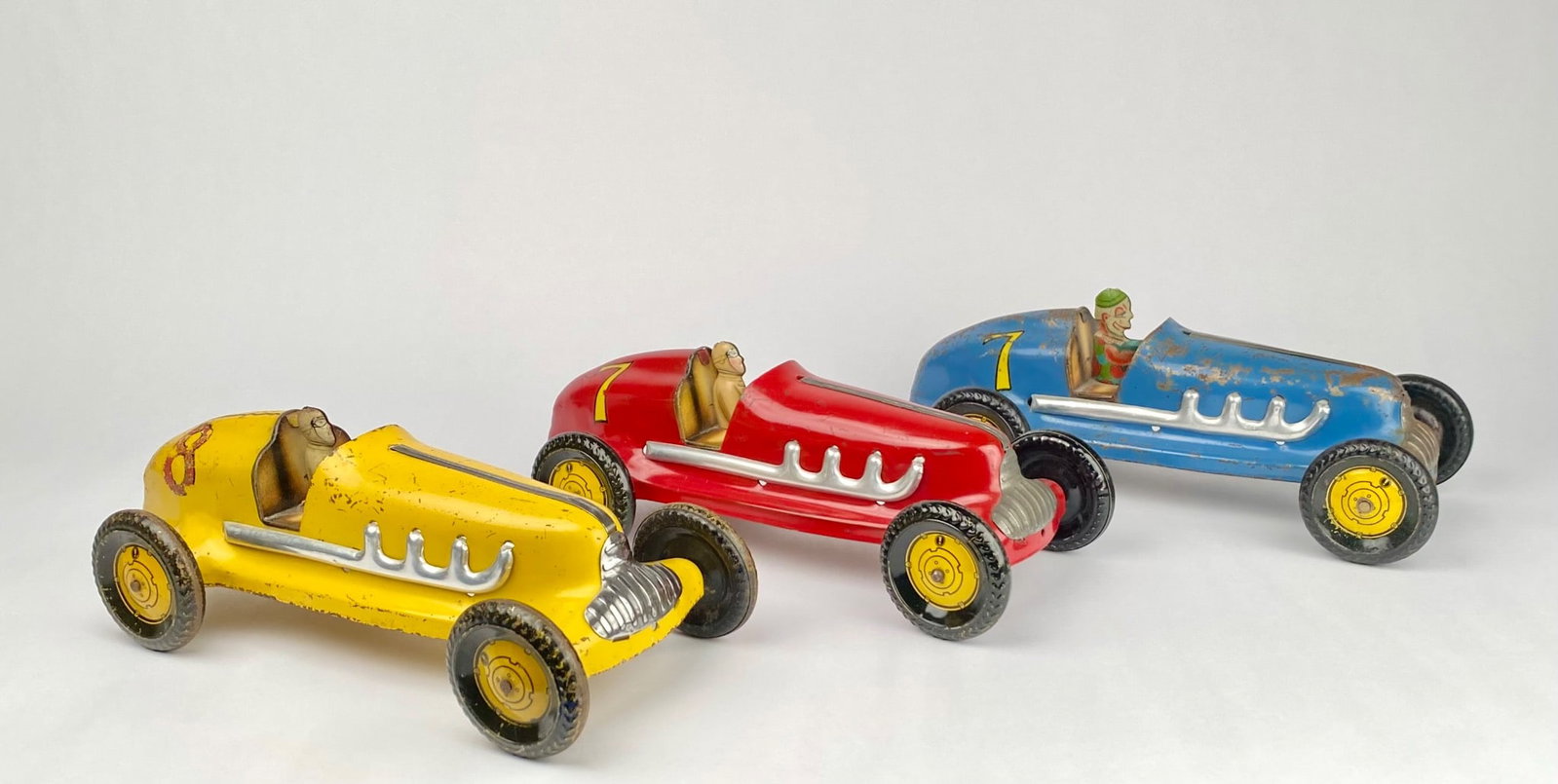 Lot of 3 Vintage Pressed Steel Racing Cars, Made in USA: Three tin toy race cars in yellow, red, and blue with driver figures. Each car features detailed trim, spoked wheels, and driver compartments. Marked "Made in USA" and exhibiting vibrant paint colors 