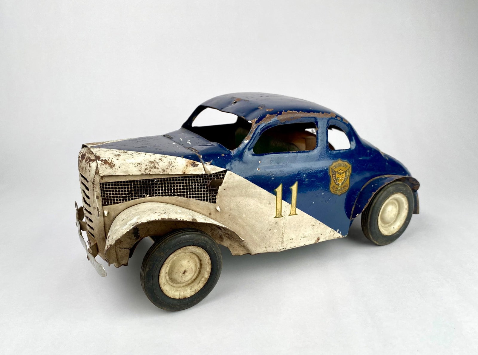 Vintage Argentine Road Race Coupe Pressed Steel Stock Car #11: Pressed steel Argentine road race coupe featuring a blue and white painted exterior with yellow number "11" decals on both sides. Includes detailed elements such as shield insignias, flexible tubing, 