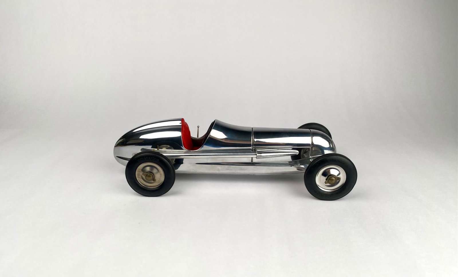 Modern Reproduction Indianapolis-Style Chrome Tether Car Model With Box: Chrome-plated model race car featuring "Indianapolis"-marked wheels, a sleek aerodynamic design, and a red interior. The car includes intricate detailing inside the cockpit, such as a steering wheel a