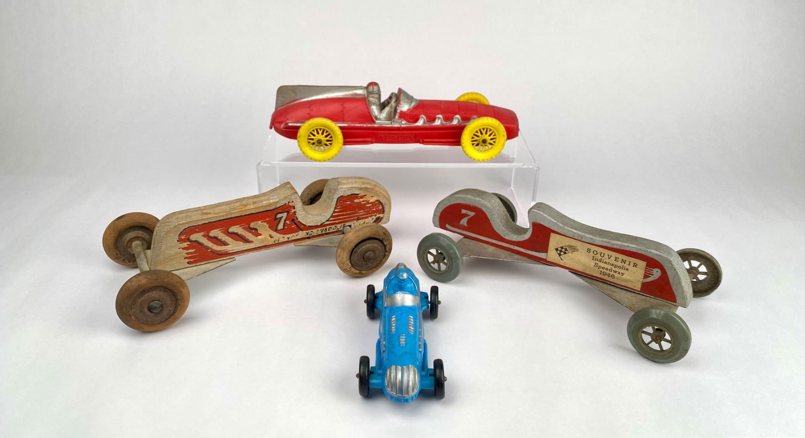 Lot of 4 Vintage Indy Racing Toys (1946 Souvenirs & Auburn Cars): Four vintage racing cars, including two wooden hand-crafted derby cars with painted details, one marked with number "7", and metal plate bases. The lot also includes two plastic racing cars: a red Aub