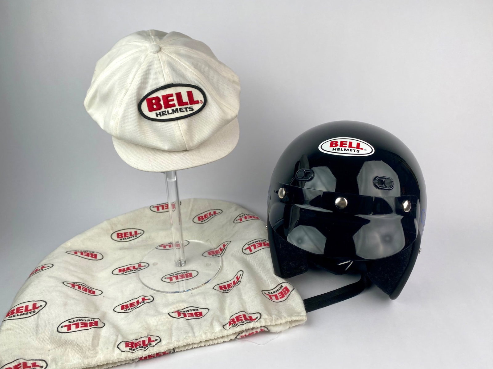 Bell Helmets Vintage Racing Helmet, Cap and Carrying Bag Set: Three-piece Bell Helmets racing set that includes a black gloss open-face helmet with Bell logo decals, a flip-up visor, and strap, featuring an autograph sticker on the sides. The interior padding an