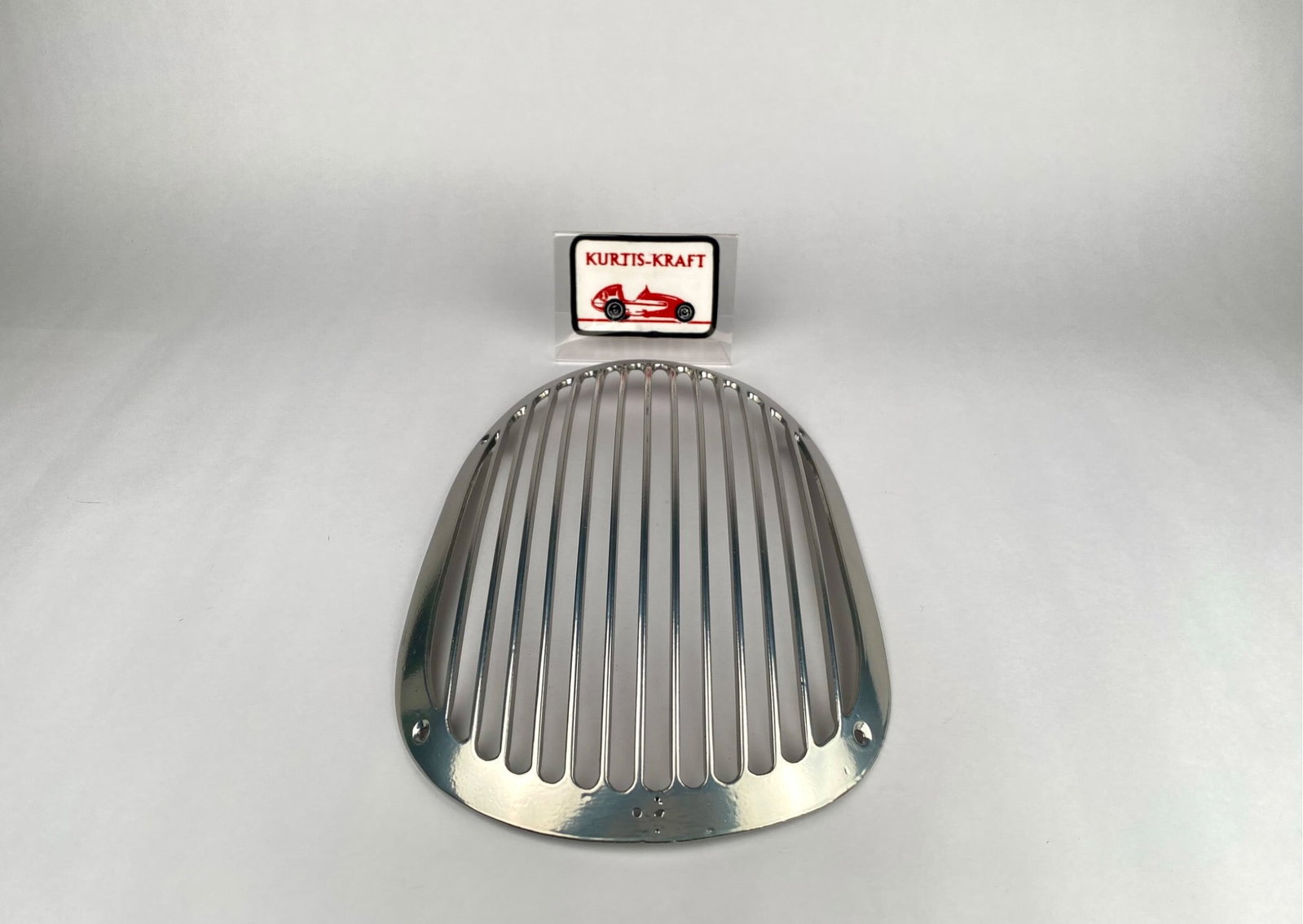 Kurtis-Kraft Style Polished Metal Grille with Display Patch: Polished metal grille in the style of Kurtis-Kraft, featuring a sleek design with horizontal slats and pre-drilled holes for placement. Includes a Kurtis-Kraft display patch presented in a protective 