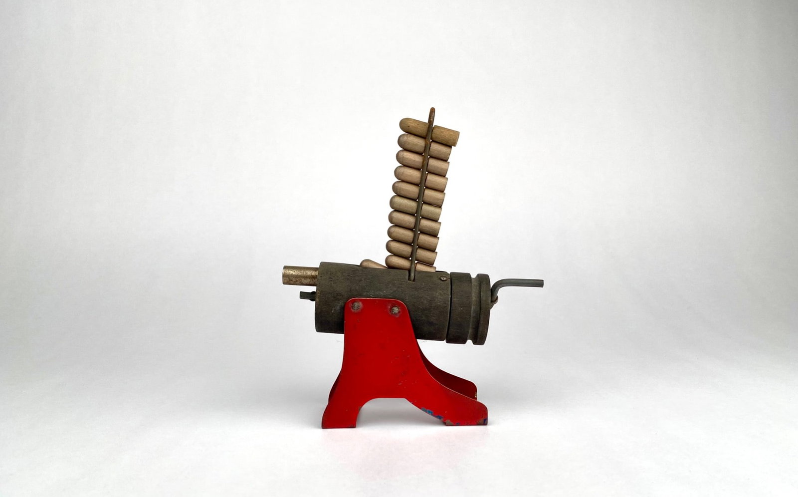 Vintage Aden 'Rapid Fire' Toy Gun with Wooden Ammunition: Vintage Aden toy gun made from metal and wood. Features a red painted metal stand and a rotating drum mechanism. Includes wooden bullets loaded into a vertical metal rack. The piece shows signs of wea