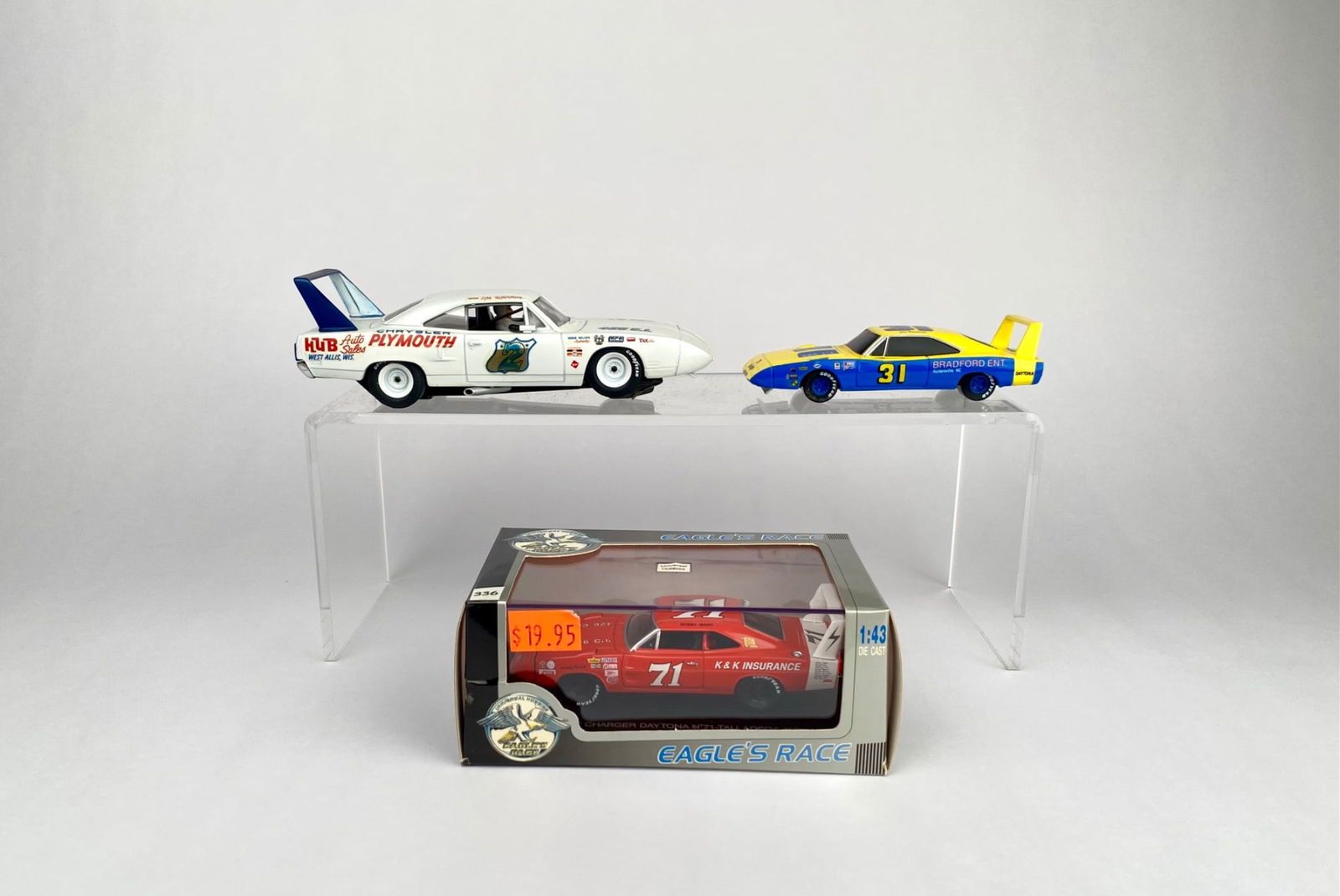 3 Die-Cast Racing Cars; Dodge Charger and Plymouth Superbird: Three die-cast models, featuring two Dodge Daytona cars and one in original packaging marked "Eagle's Race, Serie Legende." The packaged car is a red 1:43 scale Dodge Charger Daytona #71 with K & K In