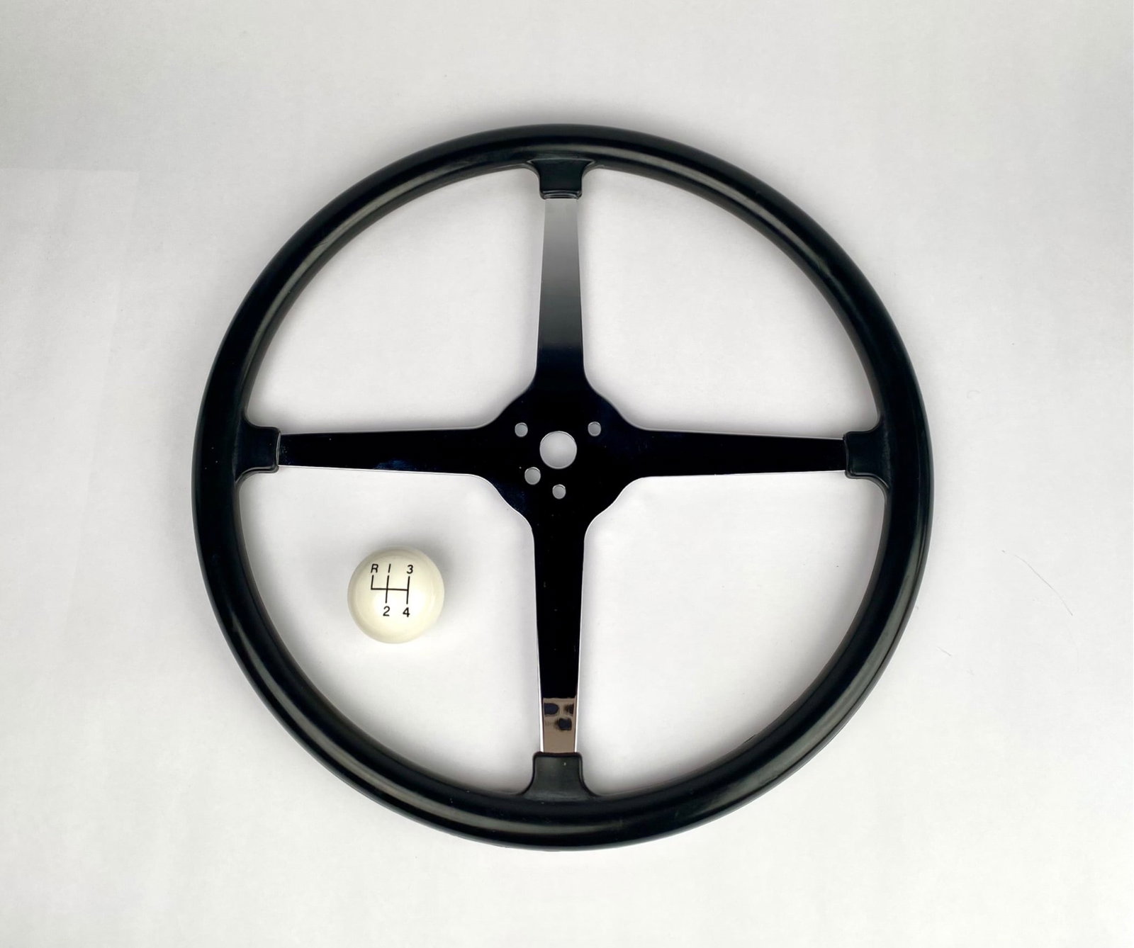 Black Four-Spoke Steering Wheel and White Shift Knob: Black four-spoke steering wheel featuring chrome detailing with part number UP#110124 stamped on the center. Accompanied by a white manual transmission shift knob labeled with a four-speed gear patter