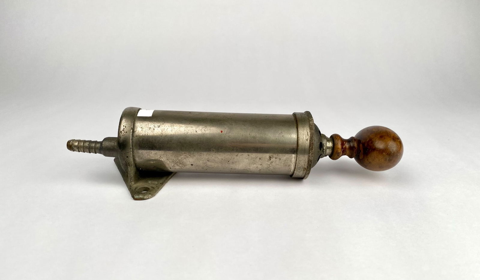 Vintage Metal Air Pump with Wood Handle: Metal hand-crank air pump featuring a cylindrical body and a wooden handle. The body includes a mounting plate with three drilled holes for attachment. Wear, oxidation, and surface imperfections are v