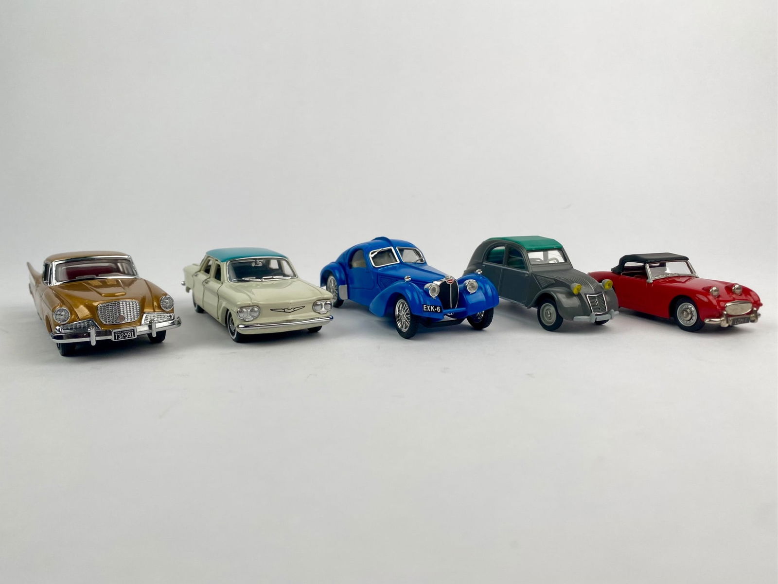 Collection of Five Vintage 1:43 Scale Die-Cast Cars: Lot includes five die-cast cars from various makers and eras. Featured is a 1956 Studebaker Golden Hawk in gold by Dinky/Matchbox (1991), a blue Bugatti Atlantic by Brumm, a white Chevrolet Corvair wi