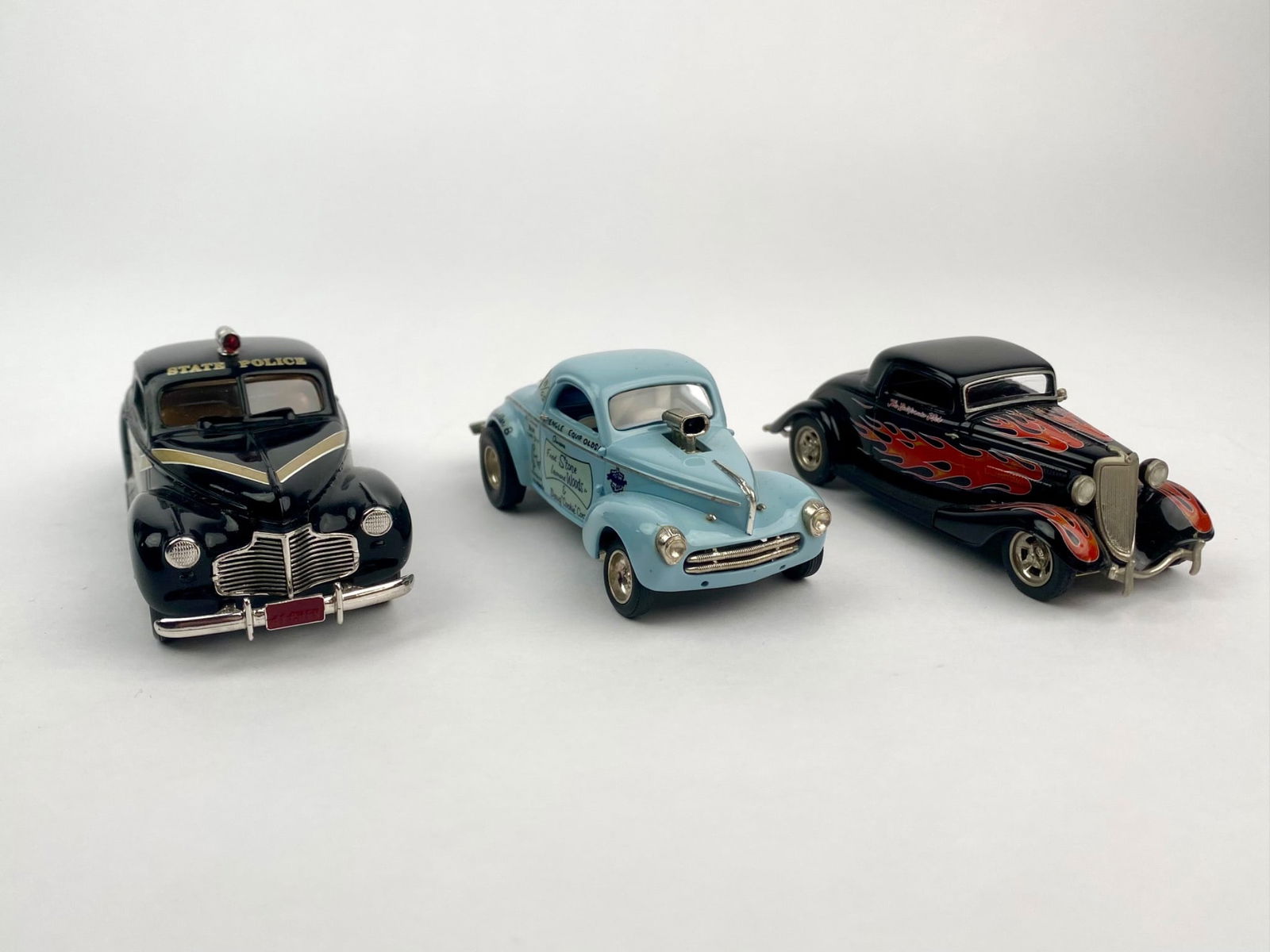 Three Die-Cast Model Cars -1941 Chevrolet, 1941 Willys, and 1934 Ford Coupe: Set includes three 1:43 scale die-cast cars with detailed period styling. The first is a 1941 Chevrolet Deluxe Coup "Michigan State Police," marked "Durham Classics Oshawa Canada" on the base. The sec