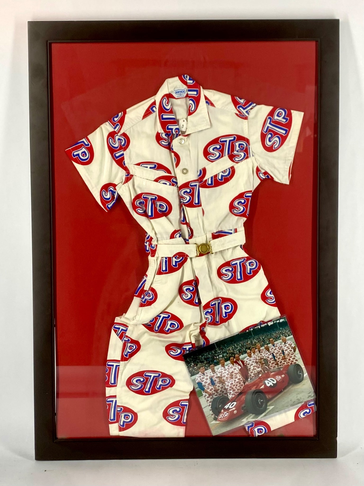 Framed Vintage STP Racing Team Uniform with Photograph: Framed vintage STP racing team uniform featuring the red, white, and blue STP logo in an all-over print. Manufactured by Artex, the short-sleeve jumpsuit includes its original belt and is mounted agai