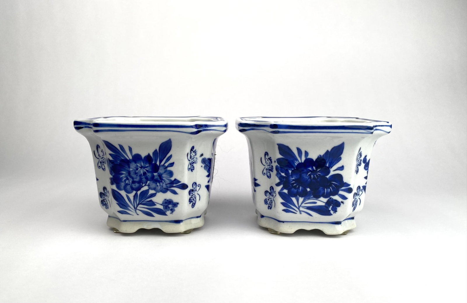 Blue and White Chinese Porcelain Planters with Floral Motif: Blue and white Chinese porcelain planters, each featuring a floral motif with butterflies. The square shape includes scalloped bases and hand-painted detailing in cobalt blue. Some wear is consistent 
