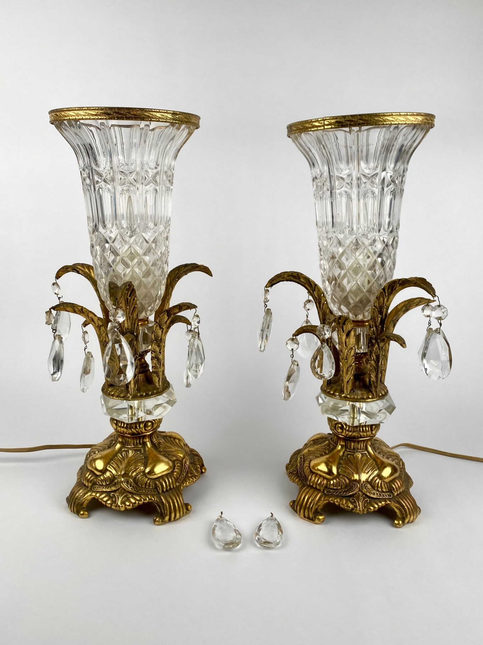 Pair of Vintage Crystal and Gilt Metal Manel Lamps with Prisms: Pair of vintage electric mantel lamps featuring cut crystal trumpet-form shades with gilt metal mounts and ornate bases. Each lamp is adorned with faceted crystal prisms suspended from gilt foliate ar
