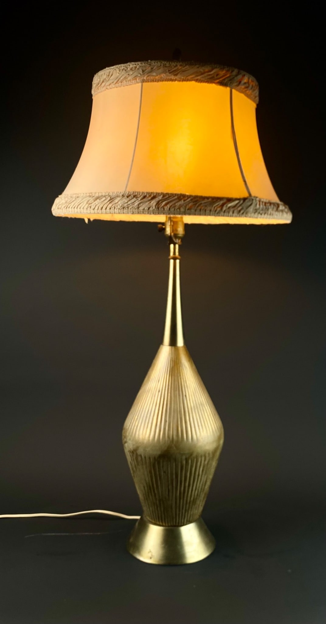 Brass Mid-Century Table Lamp with Fabric Shade: Brass mid-century table lamp featuring a ribbed, sculptural base and a fabric shade with decorative trim. Includes original finial and wiring. The shade exhibits minor wear consistent with age. The la