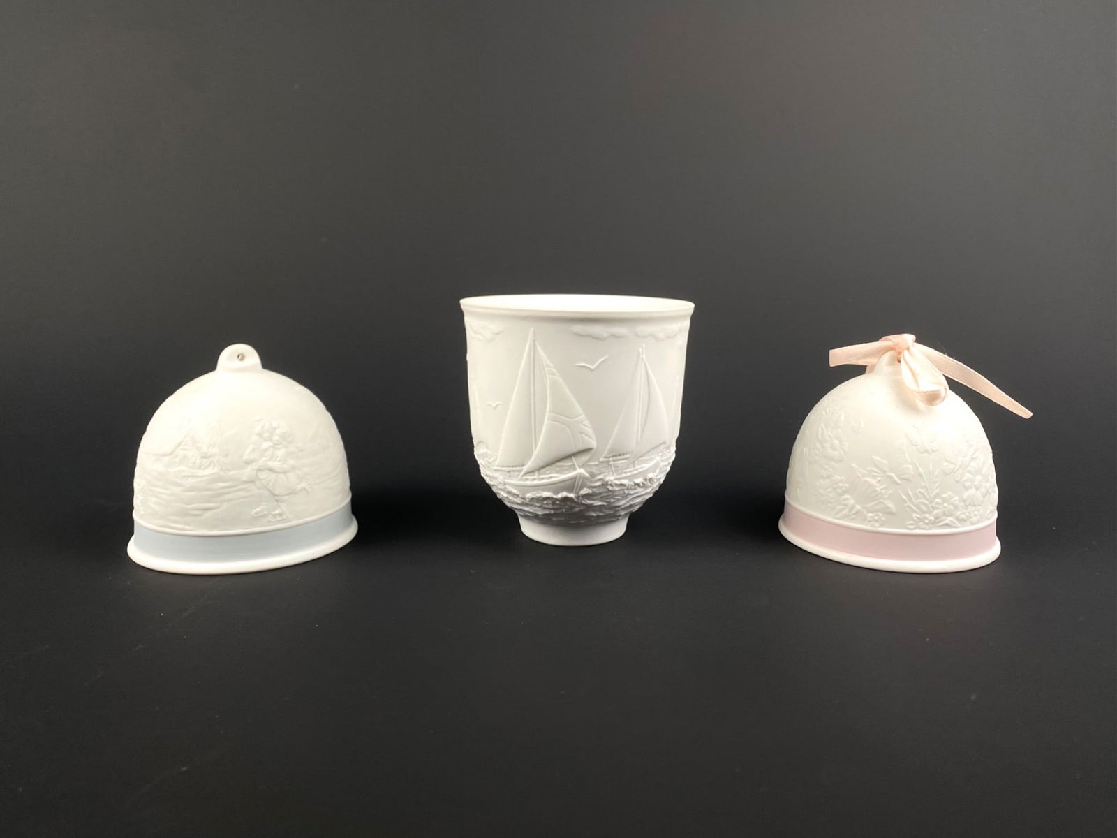 Set of Two Llardo Collector Society Bells (91 & 94) & 1997 Sailboat Votive: Set of three Llardo porcelain pieces from the Lladro Collector's Society, including two bisque porcelain bells and one votive holder. The 1991 bell depicts a floral motif with butterflies, accented by