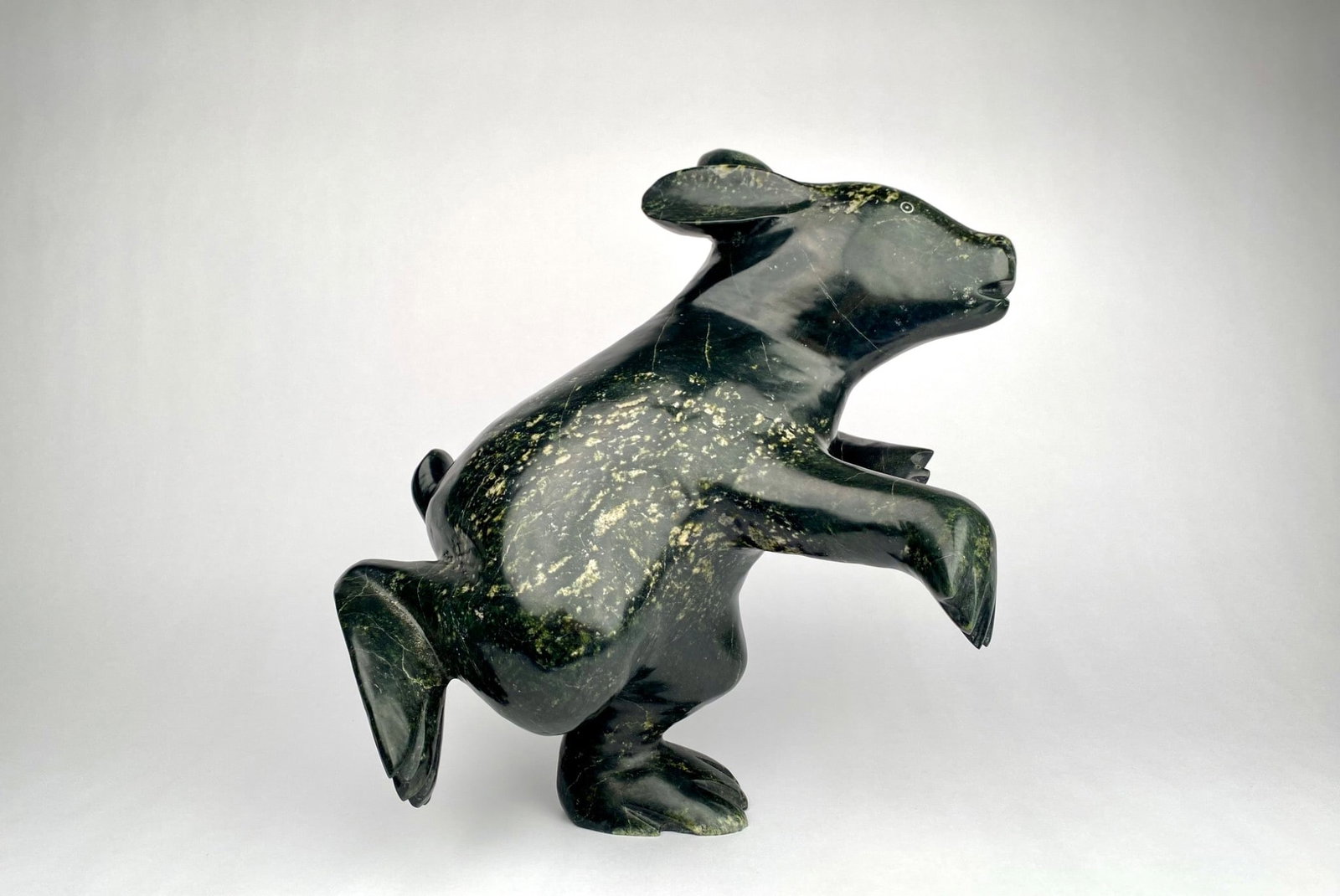 Kelly Qimirpik (Inuit, Kinngait) 'Dancing Rabbit' Serpentine Sculpture: Hand-carved serpentine sculpture of a dancing rabbit by Inuit artist Kelly Qimirpik of Kinnagait, Nunavut. The carving depicts a rabbit in a upright pose with raised arms and carved feet, conveying mo