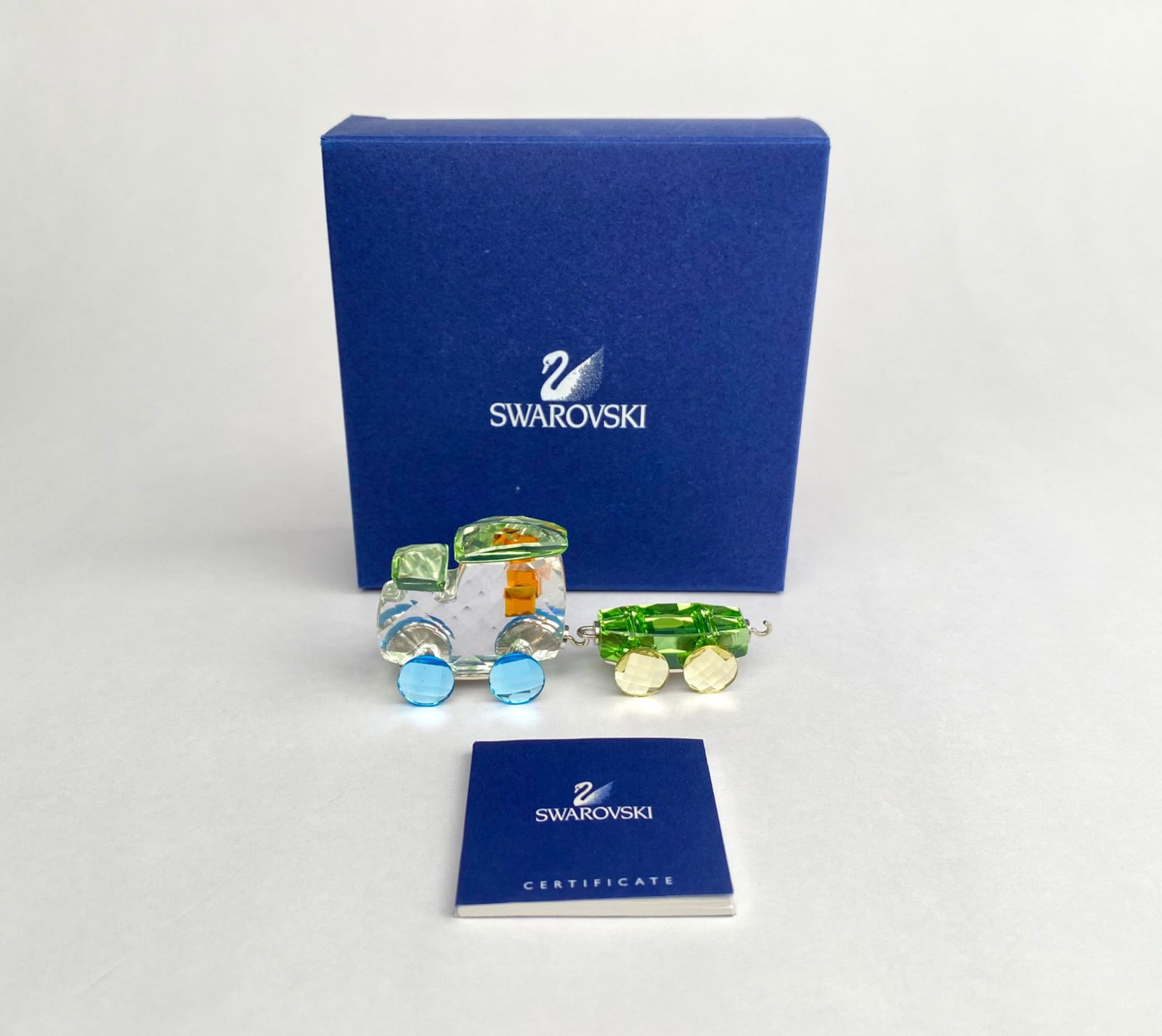 Swarovski ‘Tim the Train’ Crystal Train with Certificate and Box: Swarovski crystal decorative train, featuring a locomotive and one wagon. Includes box and original certificate. Crafted in Swarovski crystal with green, blue, yellow, and orange accents. Both pieces