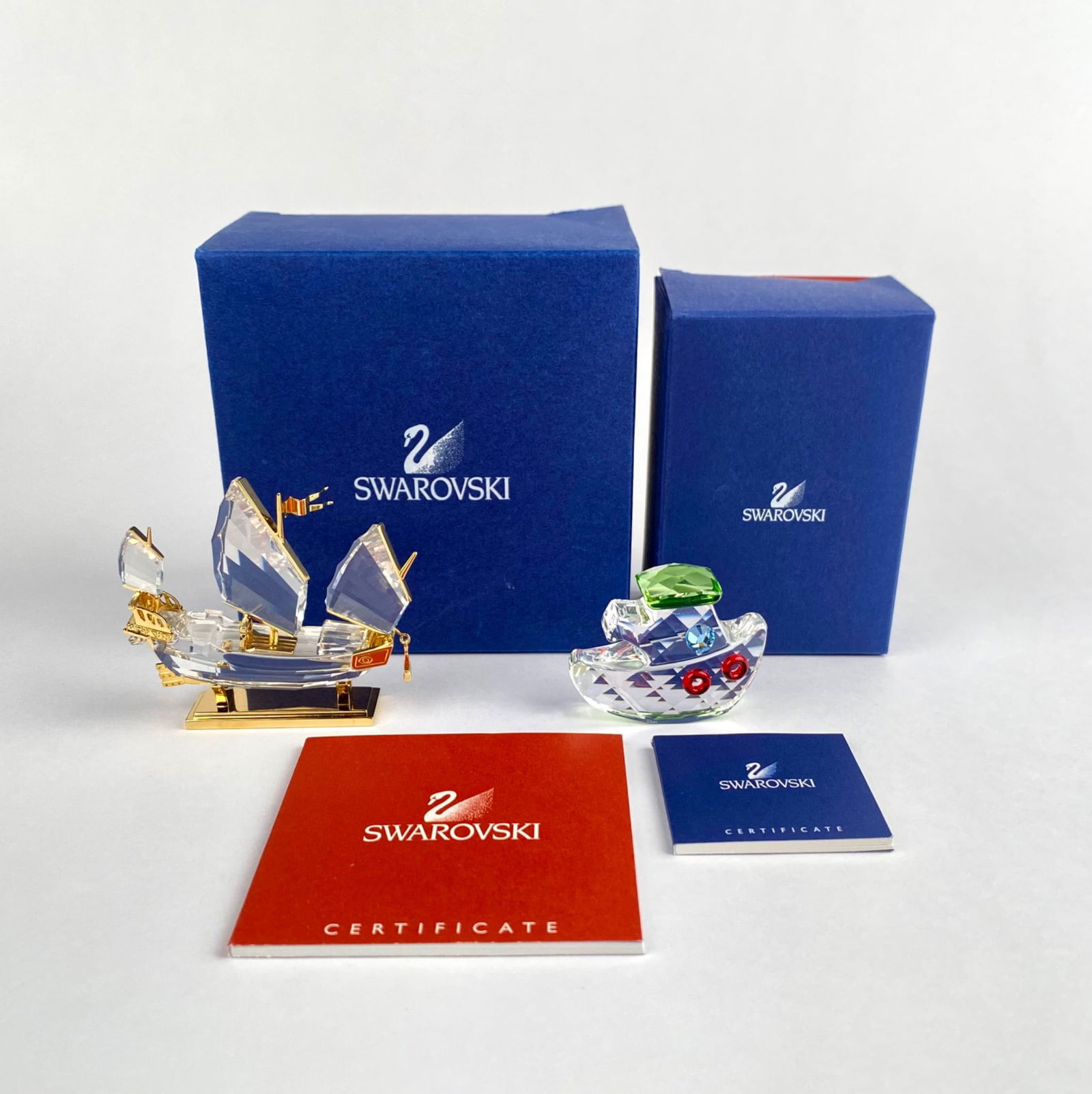 Swarovski Crystal ‘Chinese Junk’ and ‘Tugboat’ Figurines with Certificates and Boxes: Swarovski crystal 'Chinese Junk' and 'Tugboat' figurines accompanied by original boxes and certificates. The sailboat features gold-tone accents and intricate detailing, while the tugboat includes col