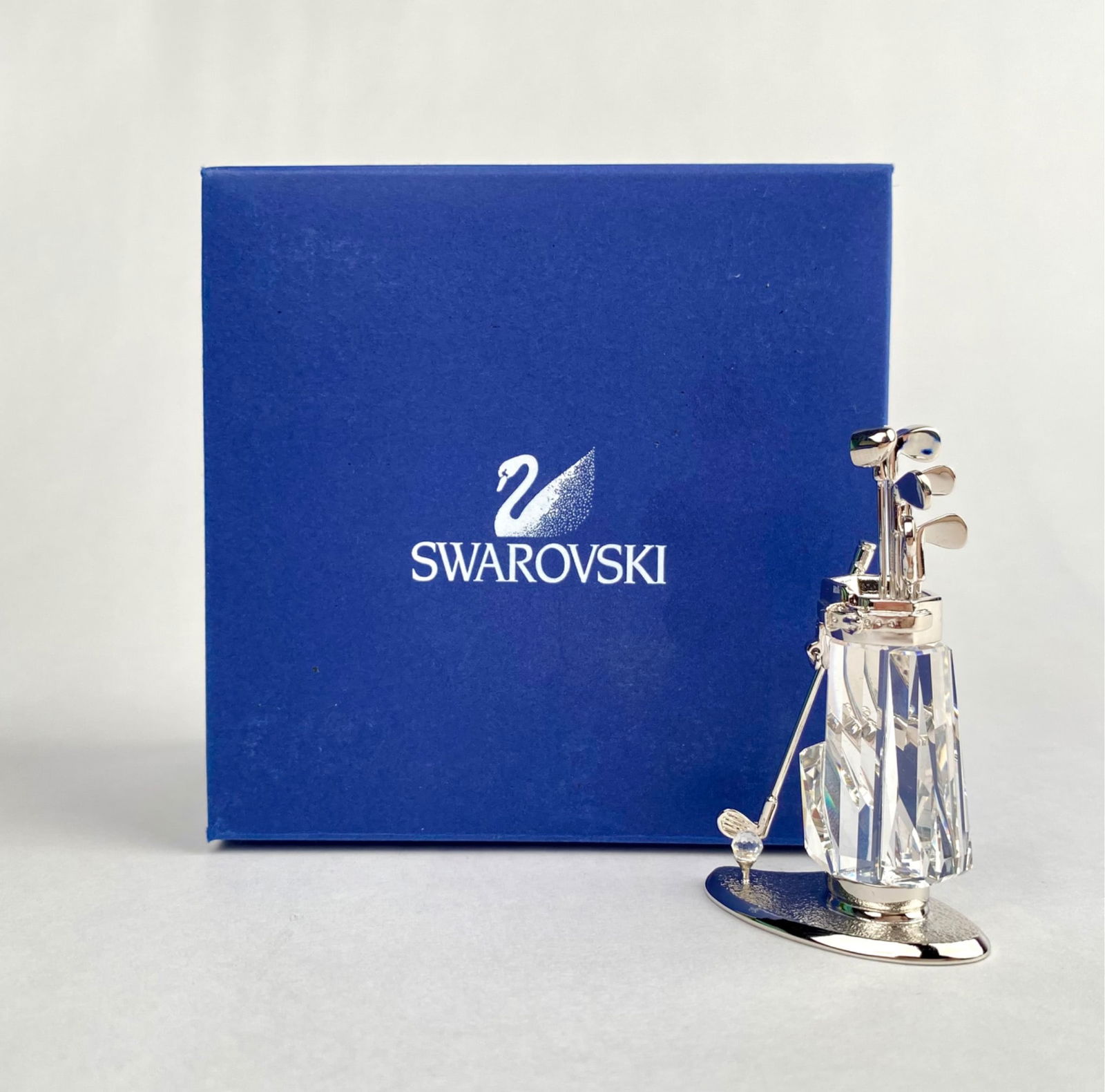 Swarovski Crystal Golf Bag with Original Box: Swarovski crystal golf bag featuring a faceted crystal base adorned with silver-tone metal golf clubs and bag details. The item comes with its original packaging, indicating model number, and is marke