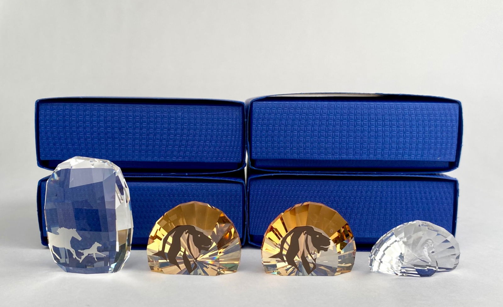 Set of Four Swarovski Crystal Animal Paperweights in Original Boxes: Swarovski crystal animal paperweights featuring animals, presented in their original boxes. Includes two amber-toned half-faceted figures with etched lions motifs, a large clear crystal piece with gal