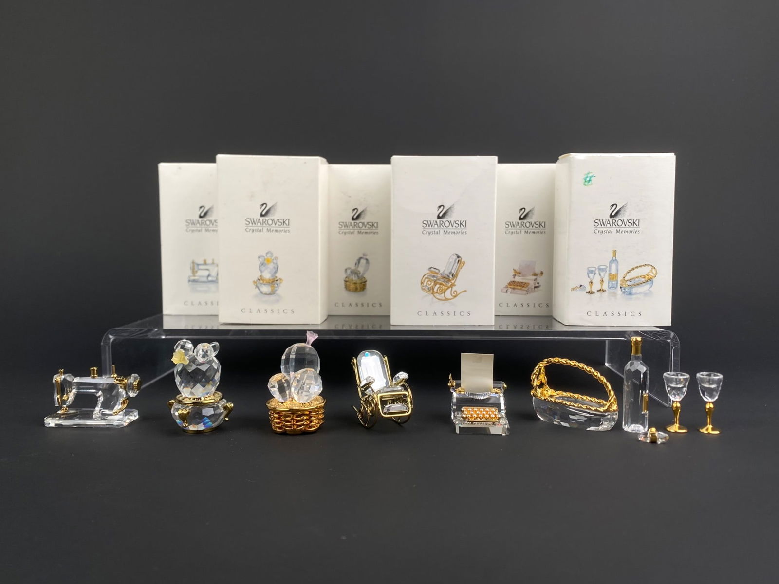 Set of Six Swarovski ‘Crystal Memories Classics’ Miniatures with Original Boxes: Set of six Swarovski "Crystal Memories Classics" miniature figurines, each accompanied by its original box. The group includes a sewing machine, rocking paper, typewriter with paper, a wine bottle set