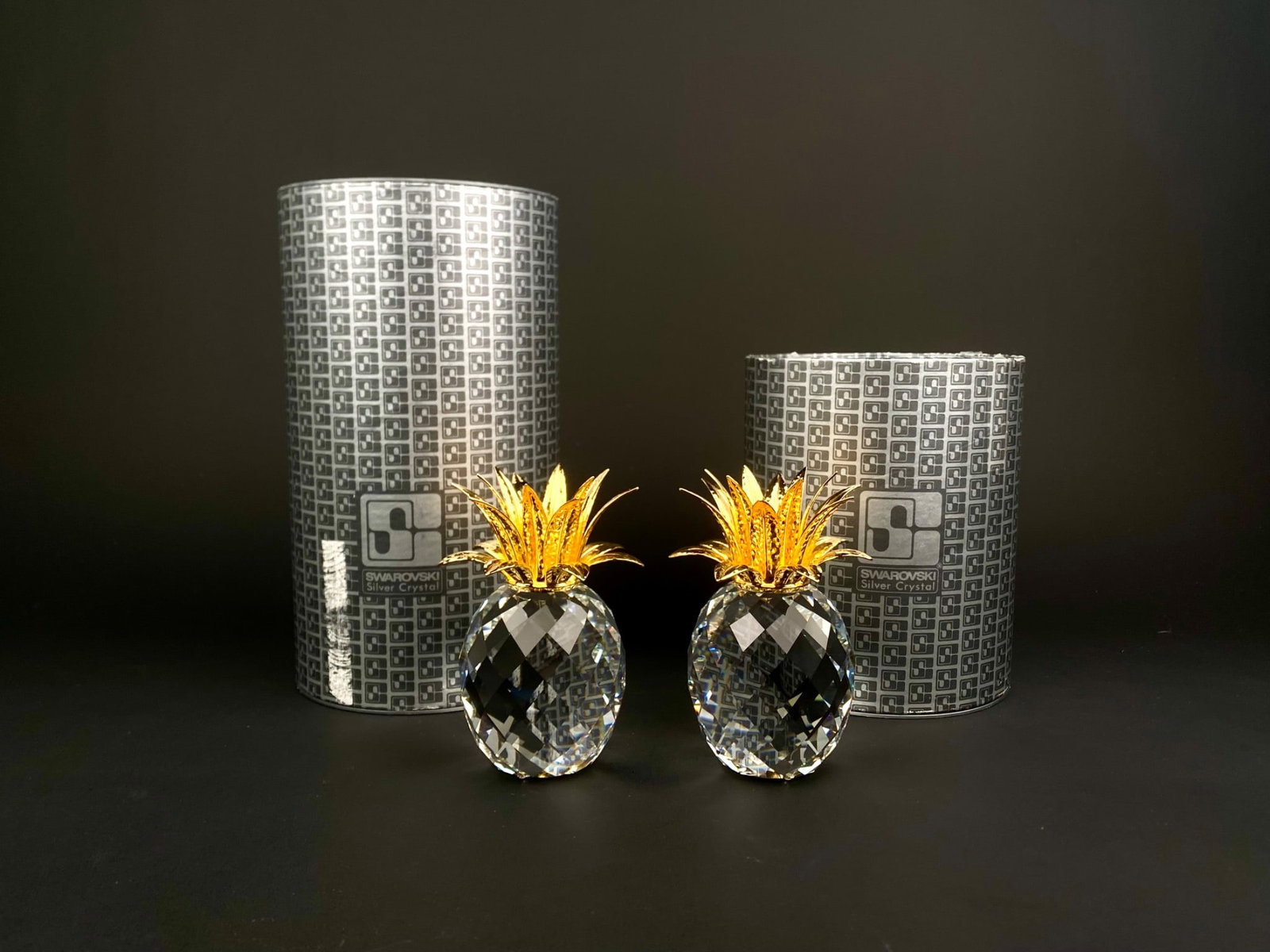 Pair of Swarovski Silver Crystal Pineapples with Original Boxes: Pair of Swarovski Silver Crystal pineapples, each crafted from faceted full-lead crystal with bright gold-tone hammered metal leaves. Both pieces display the classic Swarovski block logo etched on the
