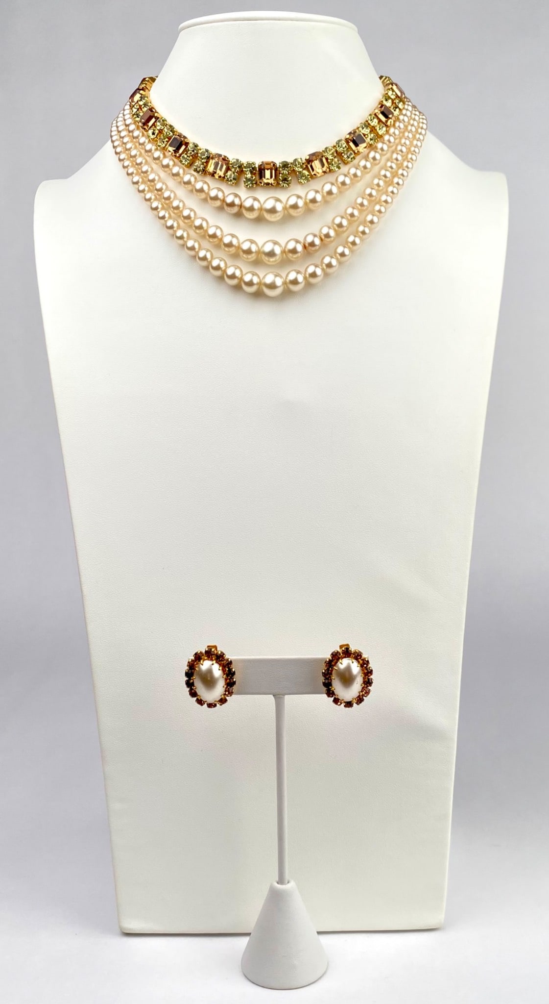 Faux Pearl Necklace and Earring Set with Austrian Hallmark: Necklace and earring set featuring multi strand faux pearls paired with gold toned metal and topaz and green rhinestone embellishments. The necklace features an adjustable clasp with a dangling faux p