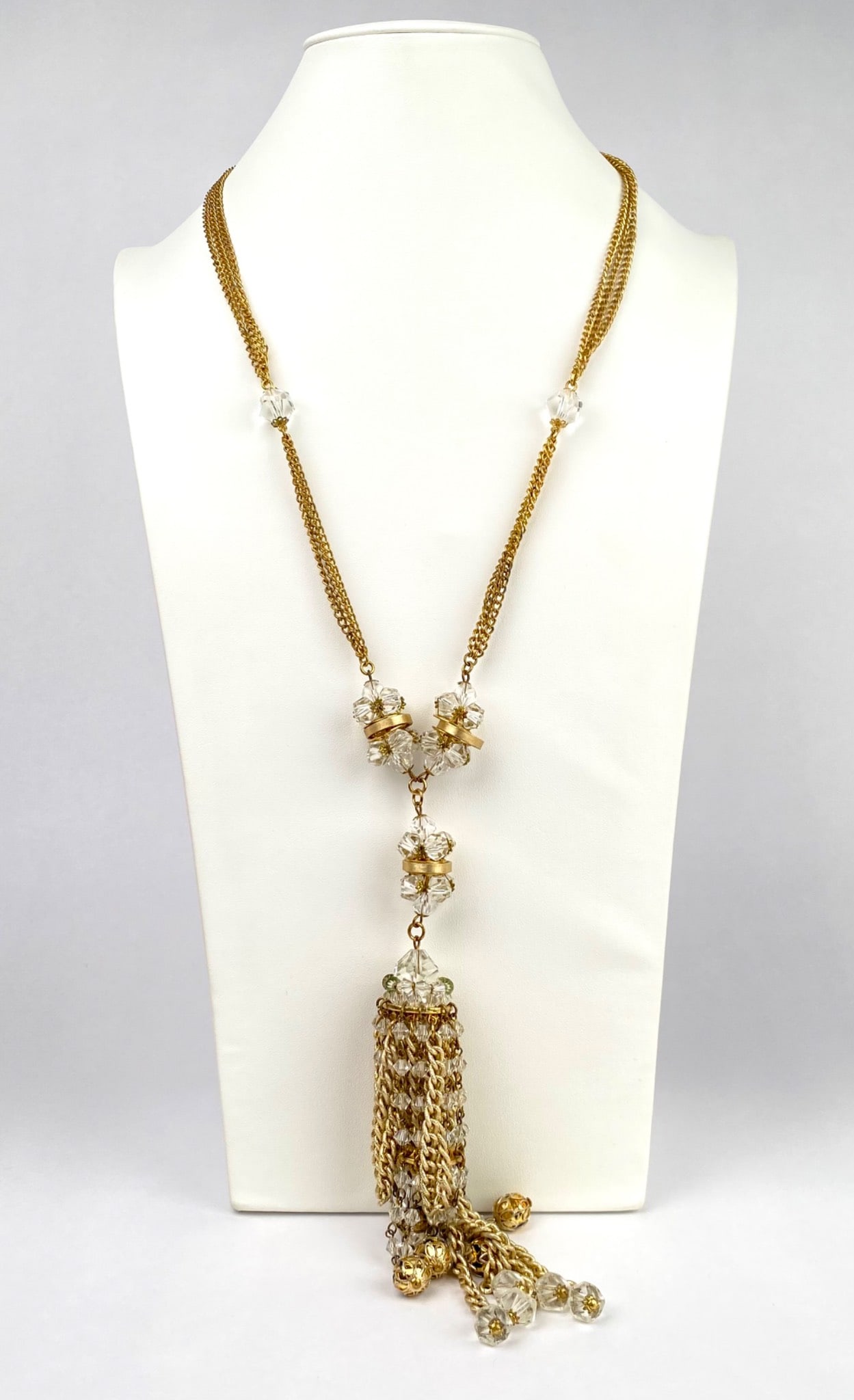 Vintage Gold Tone Tassel Necklace with Crystal Beads: Gold tone chain necklace featuring clear faceted beads and a detailed tassel pendant. The design includes gold tone filigree caps and enameled accents on select beads. The necklace fastens with a flor
