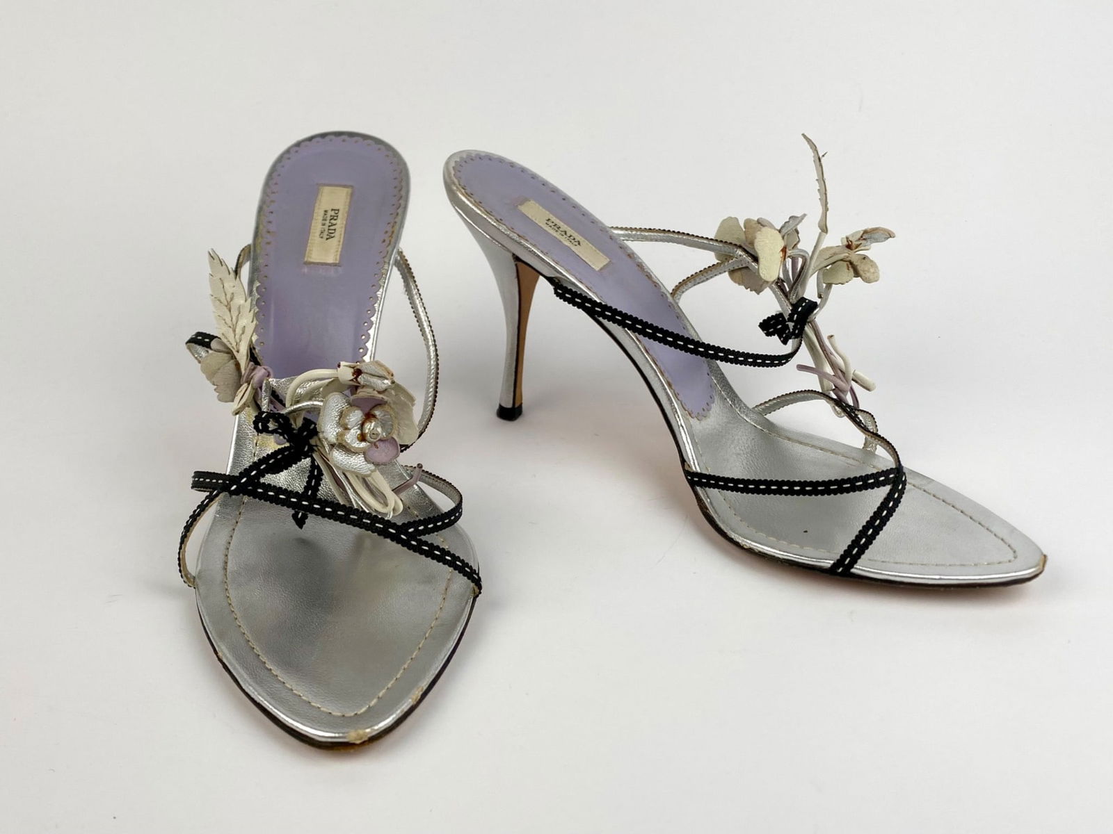 Prada Silver Leather Floral Embellished Mules, Neiman Marcus 95th Anniversary Edition, Size 38.5: Pair of limited-edition Prada mule sandals created exclusively for Neiman Marcus' 95th Anniversary. The design features metallic silver leather with black stitched straps and lilac leather insoles, ac