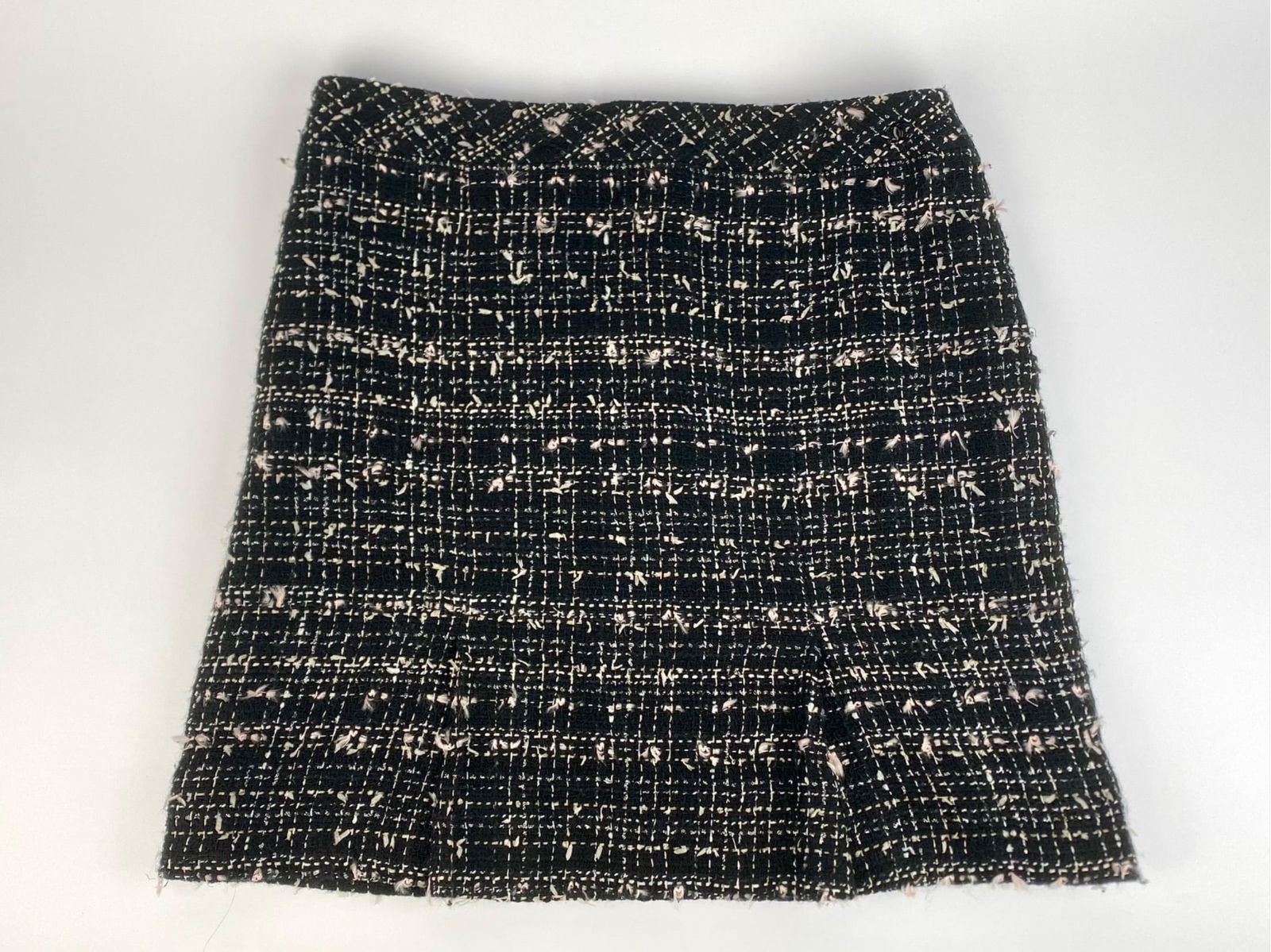 Chanel Black & Ivory Boucle Tweed Mini Skirt: Chanel black and ivory boucle tweed mini skirt featuring a classic woven texture with subtle fringe accents throughout. The skirt includes a small black CC logo embellishment at the waistband and has