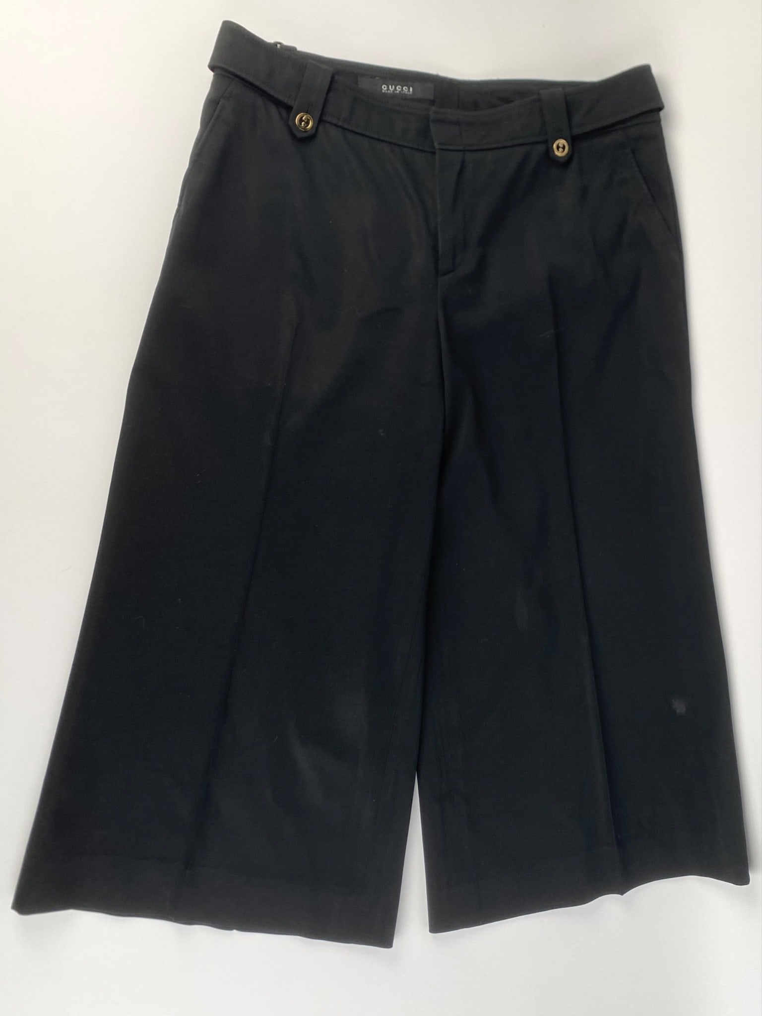 Gucci Black Cropped Wide-Leg Pants, Size 44: Pair of Gucci black cropped wide leg pants, made in Italy and marked size 44. The pants feature a mid-rise waist, belt loops, and side waist adjusted tabs finished with gold-tone GG logo buttons. The 