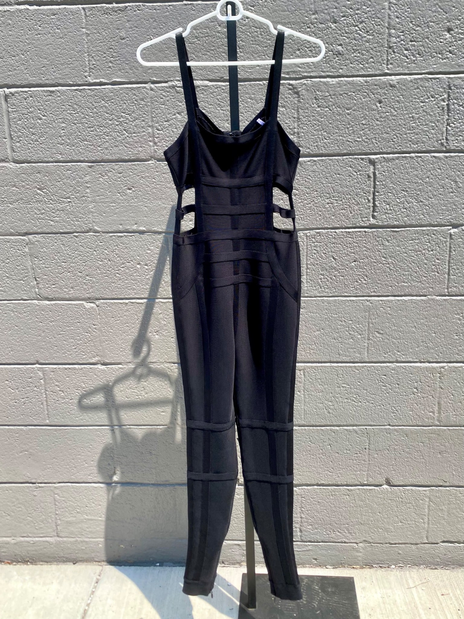 Herve Leger by Max Azria XS Black Bandage Cut-Out Jumpsuit: Herve Leger by Max Azria black bandage jumpsuit in size XS. The form-fitting design features signature bandage paneling with geometric cut-outs at the waist and a full-length silhouette with zippered