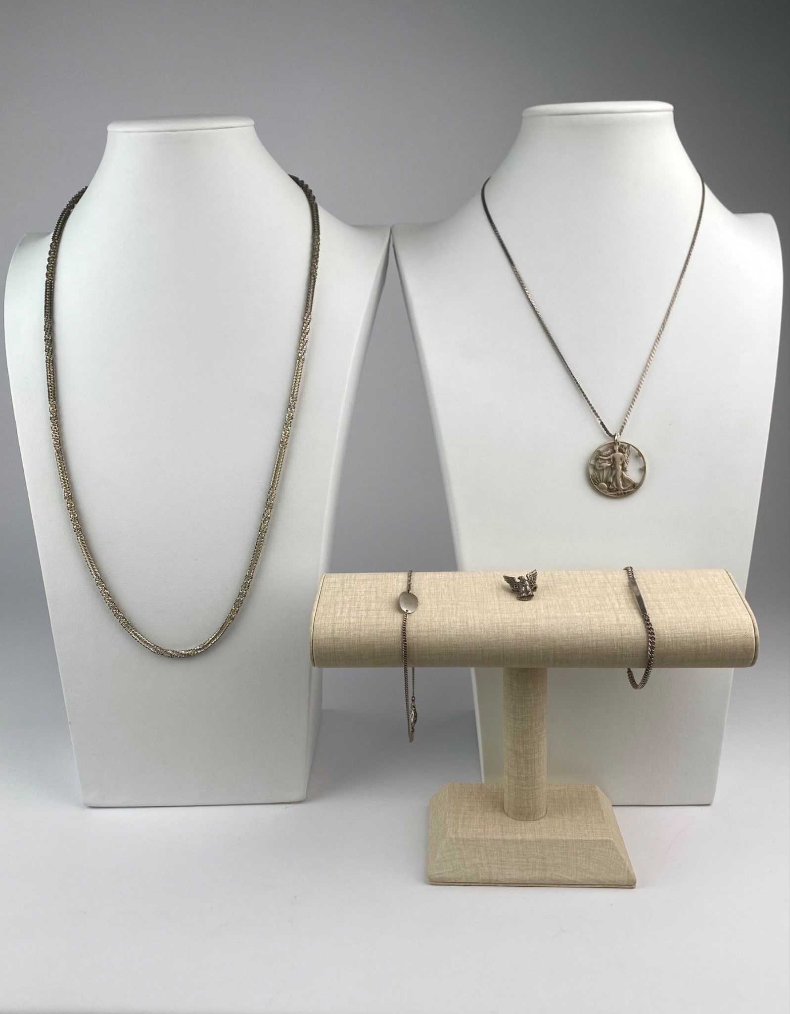 Group of Five Sterling and Silver-Tone Jewelry: Mixed lot of five silver and silver-tone jewelry pieces, primarily marked “Sterling.” The lot includes a sterling silver cutout coin pendant necklace featuring a 1942 Walking Liberty half doll