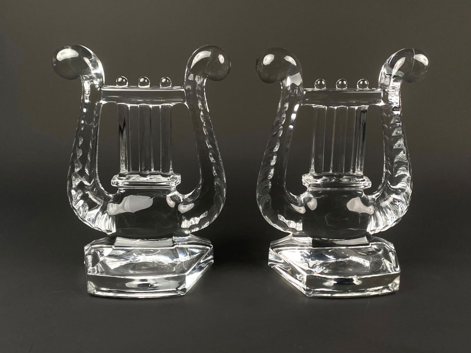 Pair of Cut Crystal Lyre Bookends: Pair of heavy clear cut crystal bookends in the shape of a classical lyre. Each piece features deeply notched scroll arms, fluted string columns, and faceted geometric bases. The reverse sides are fin
