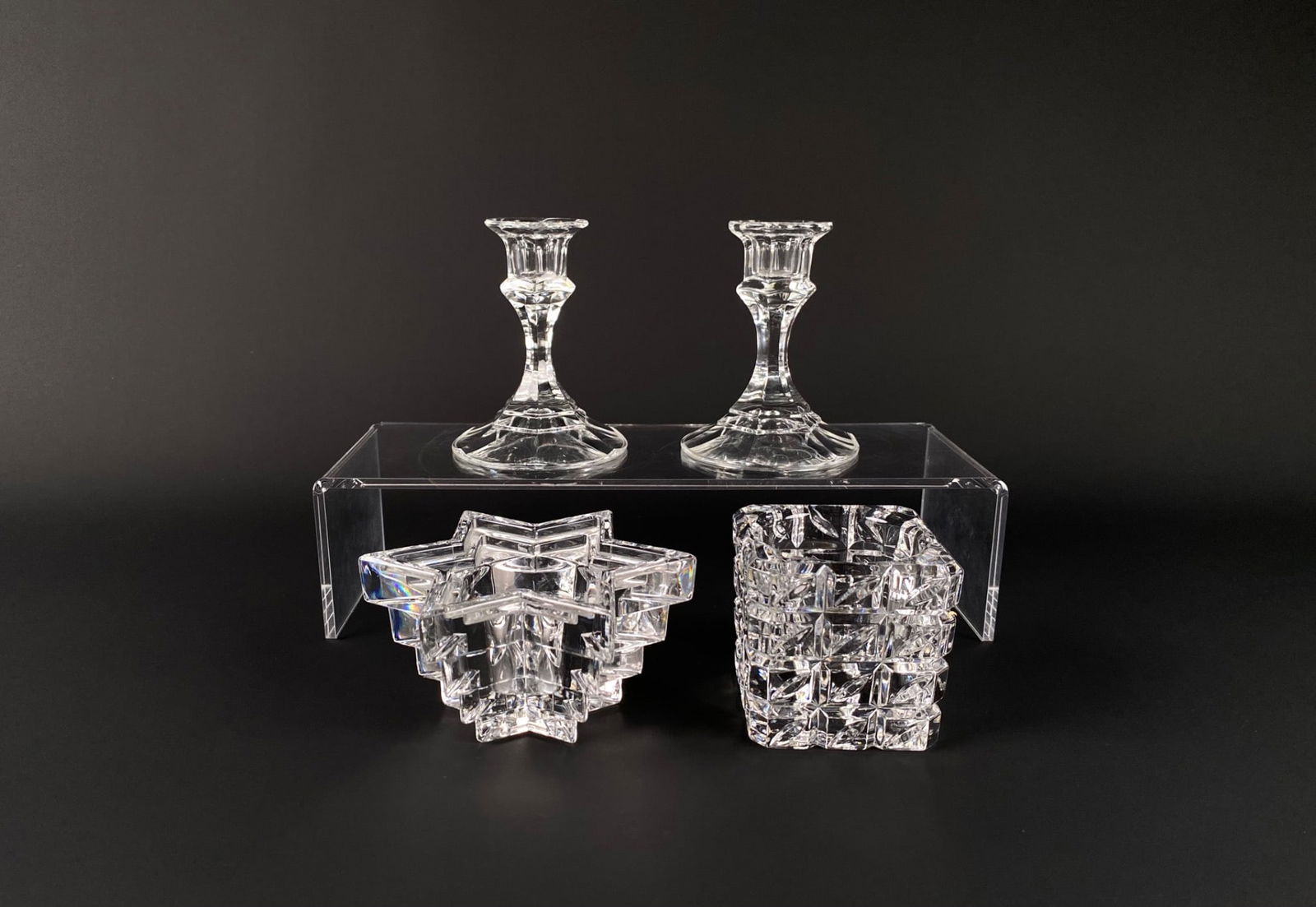 Crystal Candlesticks and Votive Holders: A pair of crystal candlesticks and two uniquely designed crystal votive holders. The candlesticks feature a traditional design, while one votive holder is star-shaped, and the other has a squared, geo