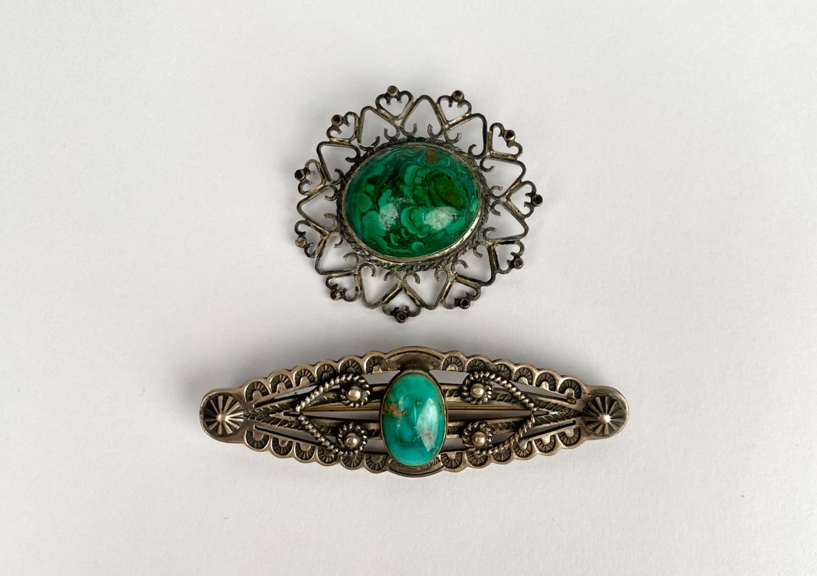 Vintage Sterling Silver Brooch Pair (Navajo Turquoise & Filigree Malachite): Two silver brooches featuring stone accents. The first brooch, a Navajo turquoise bar pin, showcases an oval turquoise stone set within a horizontal design, incorporating intricate patterns, including