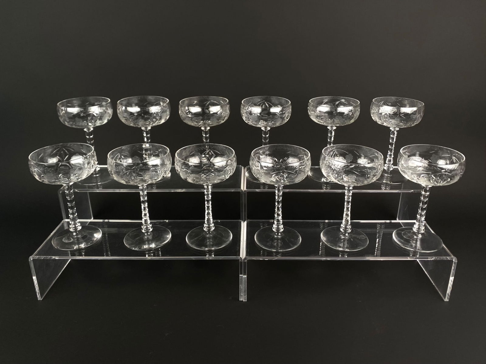 Set of 12 Hand-Cut Crystal Champagne Coupes with Faceted Stems: Set includes twelve hand-cut crystal champagne coupes, each featuring a wide bowl decorated with floral and geometric etched motifs. The design includes frosted flower clusters, diamond cartouches, an