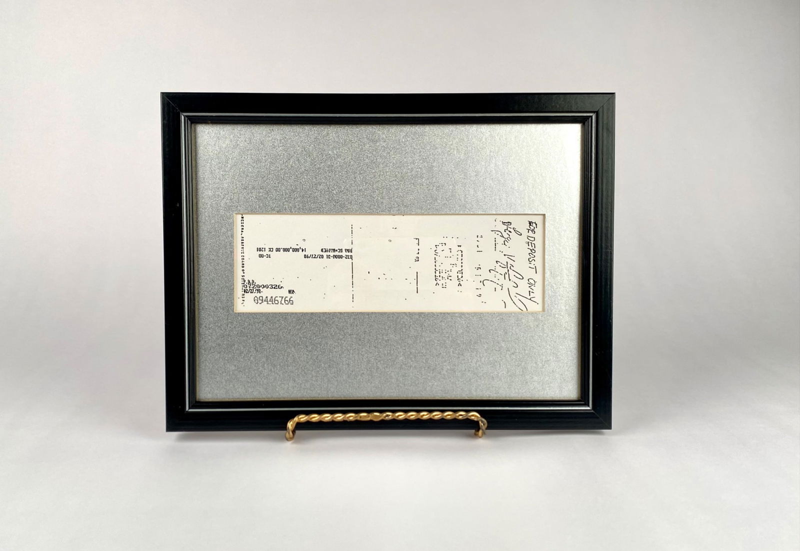 Framed Endorsed Check with Black Wooden Frame, $14,000,000 1990: Framed check mounted in a black wooden frame with a silver metallic background. The check features handwriting, stamps, and banking marks, indicating it was previously endorsed. The backside reveals a