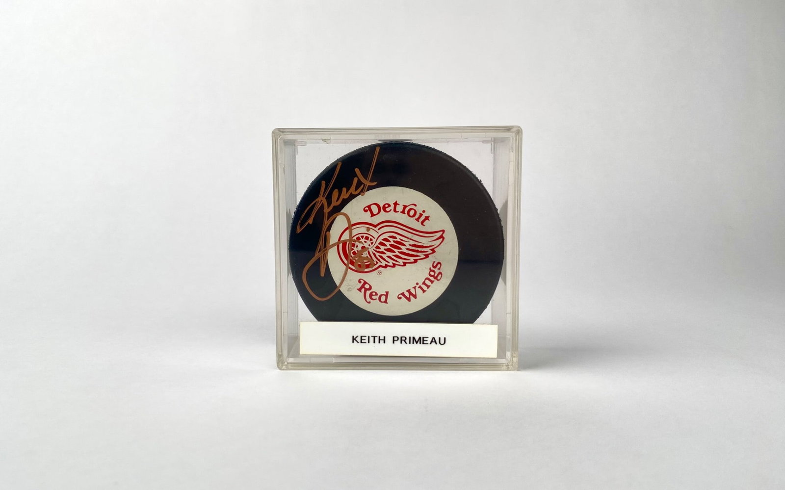 Signed Keith Primeau Detroit Red Wings Hockey Puck in Case: Official NHL licensed hockey puck featuring the Detroit Red Wings logo, signed by Keith Primeau in gold ink. The puck is housed in a clear protective display case labeled with the player’s name. Ite