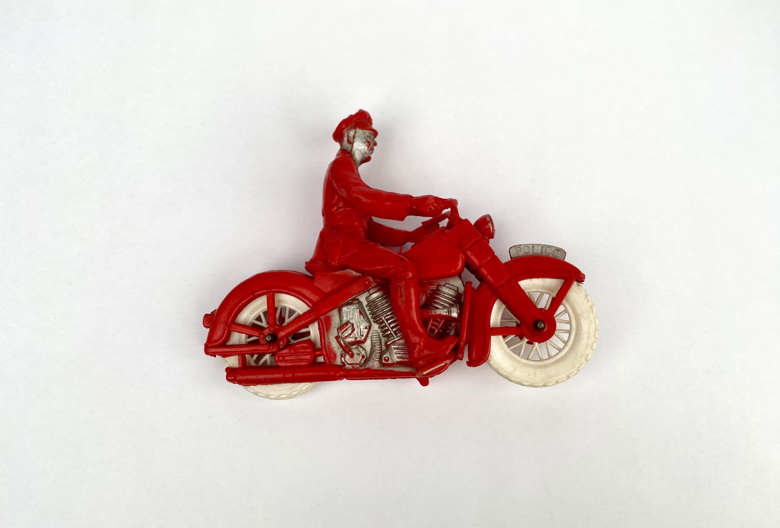 Auburn Rubber Company Red Police Motorcycle Toy with Rider: A vintage Auburn Rubber Company red police motorcycle toy featuring a rider in uniform. The toy is made of rubber and displays notable detailing, including the word ‘Police’ on the front fender an