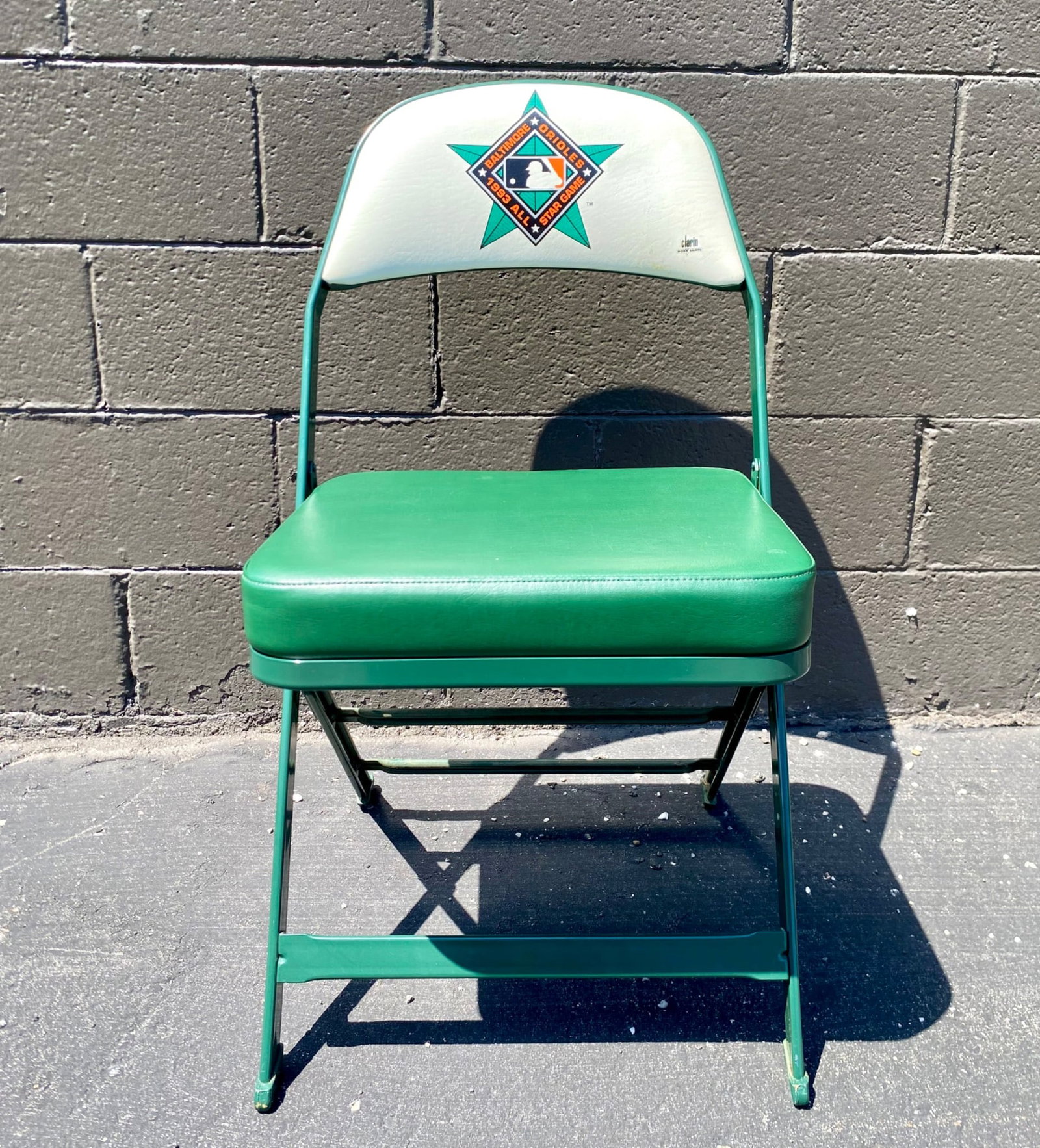 1993 Baltimore Orioles All-Star Game Folding Chair by Clarin: Clarin folding chair featuring the Baltimore Orioles 1993 All-Star Game logo prominently displayed on the white vinyl backrest. The chair is constructed with a green-painted metal frame and cushioned 