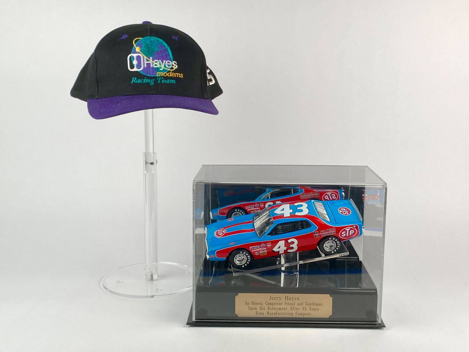 Richard Petty #43 STP Die-Cast Car with Hayes Modems Racing Team Cap: Set includes a Richard Petty #43 STP die-cast stock car displayed on a custom stand with engraved plaque, presented as a retirement gift from the Petty’s to Jerry Hayes upon his retirement. Also inc