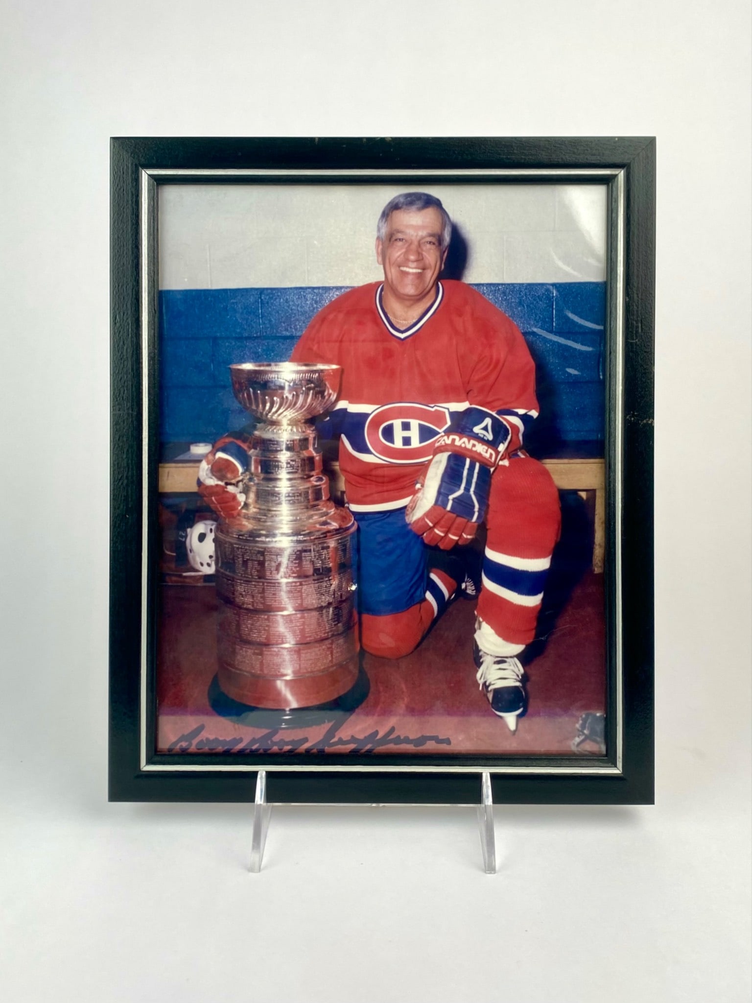 Framed Bernie “Boom Boom?? Geoffrion Signed Photo with Stanley Cup: Framed color photograph of Hockey Hall of Famer Bernie “Boom Boom” Geoffrion, shown in full Montreal Canadiens uniform kneeling beside the Stanley Cup. The image is hand-signed “Boom Boom Ge
