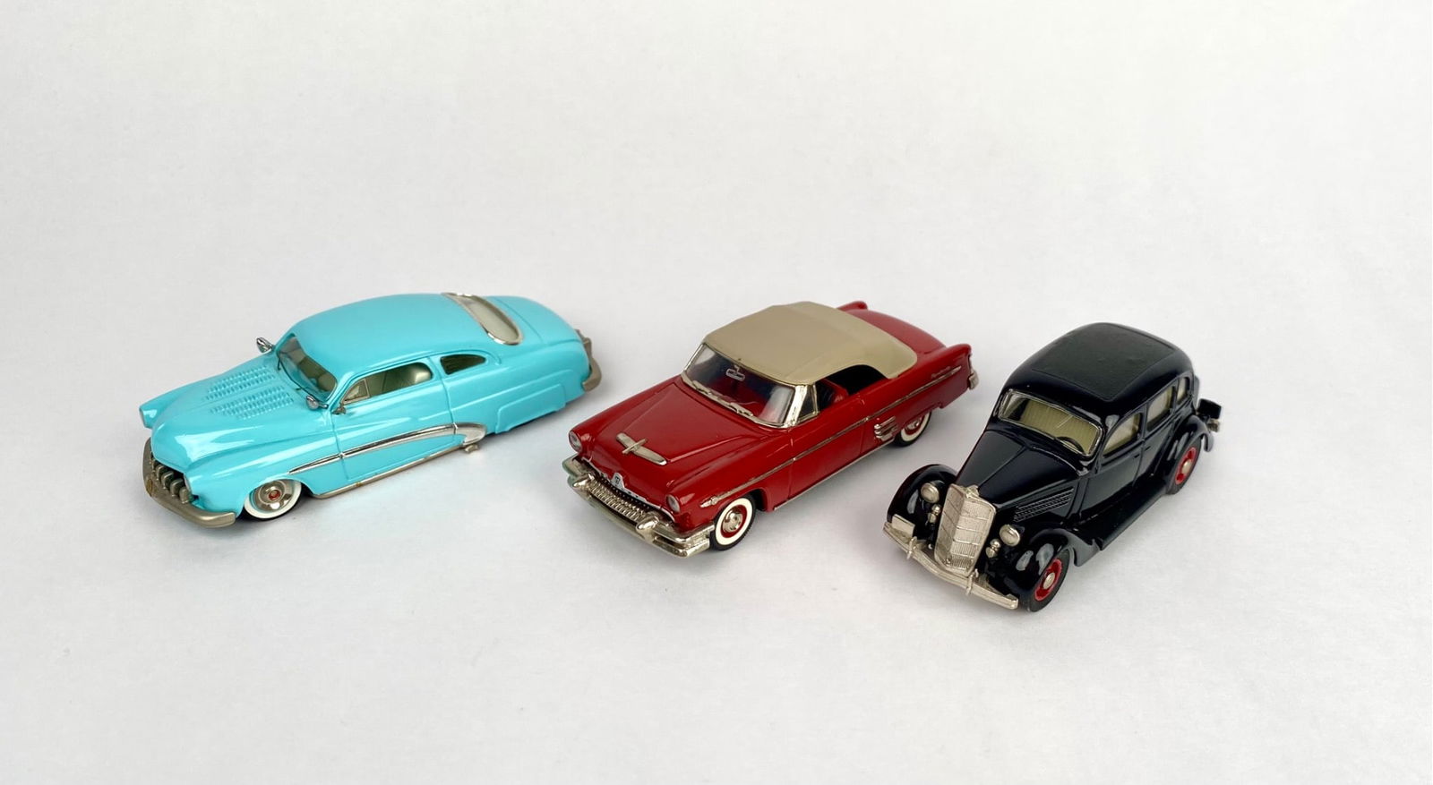 Trio of 1:43 Scale Diecast Cars; Mercury, Coupe & Ford V8: Three die-cast model cars in different colors and designs. The lot features a light blue custom 1950s-style car with silver accents, a red Mercury convertible with a tan roof, and a black vintage-styl