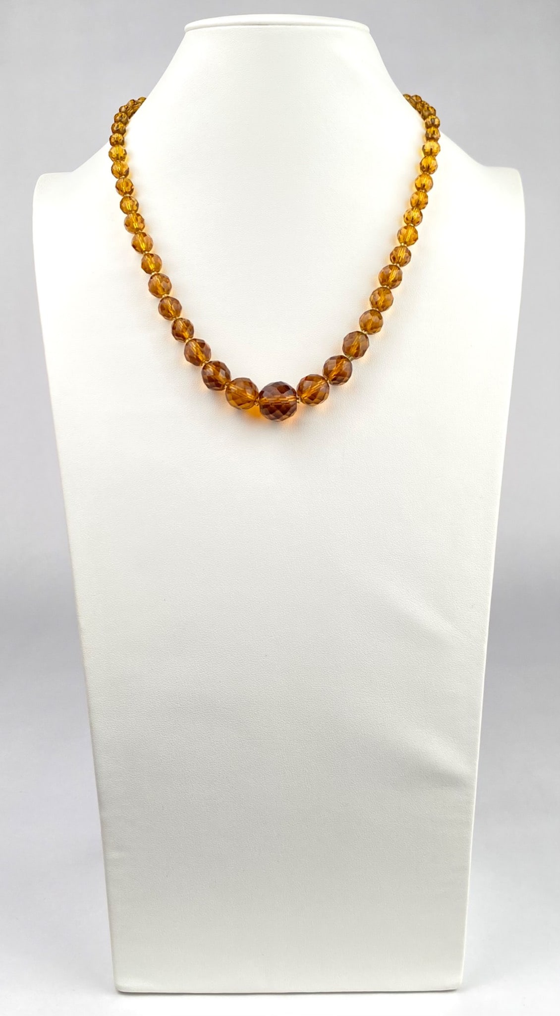 Amber Colored Faceted Crystal Necklace with Barrel Clasp: Amber colored faceted bead necklace featuring graduated bead sizes and a barrel clasp for closure. The beads are well cut, giving them a reflective finish. Necklace is in good condition. Please see ph