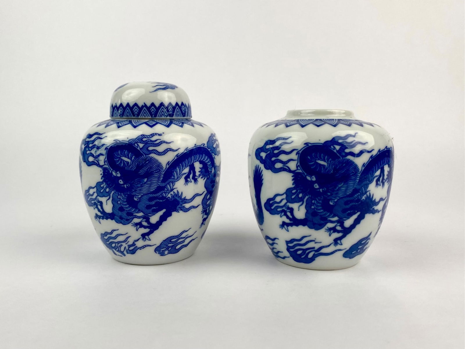 Pair of Chinese Blue and White Porcelain Dragon Jars: Set of two Chinese blue and white porcelain jars, each decorated with hand-painted dragon motifs surrounded by stylized clouds in cobalt blue. The jars feature geometric floral borders around the neck