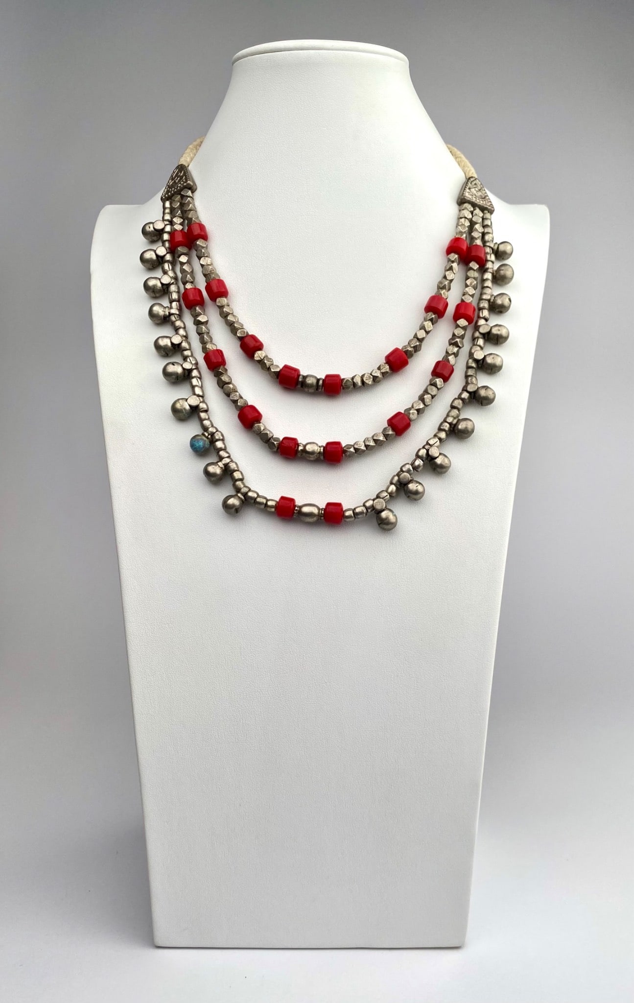 Vintage Afghan/Kuchi Mult-Strand Tribal Necklace with Silver Alloy Bells & Red Glass Beads: Silver and red beaded multi-strand necklace featuring faceted metal beads, red glass beads, and dangling metallic bead accents. Secures with a braided rope tie closure. Some signs of age-related wear