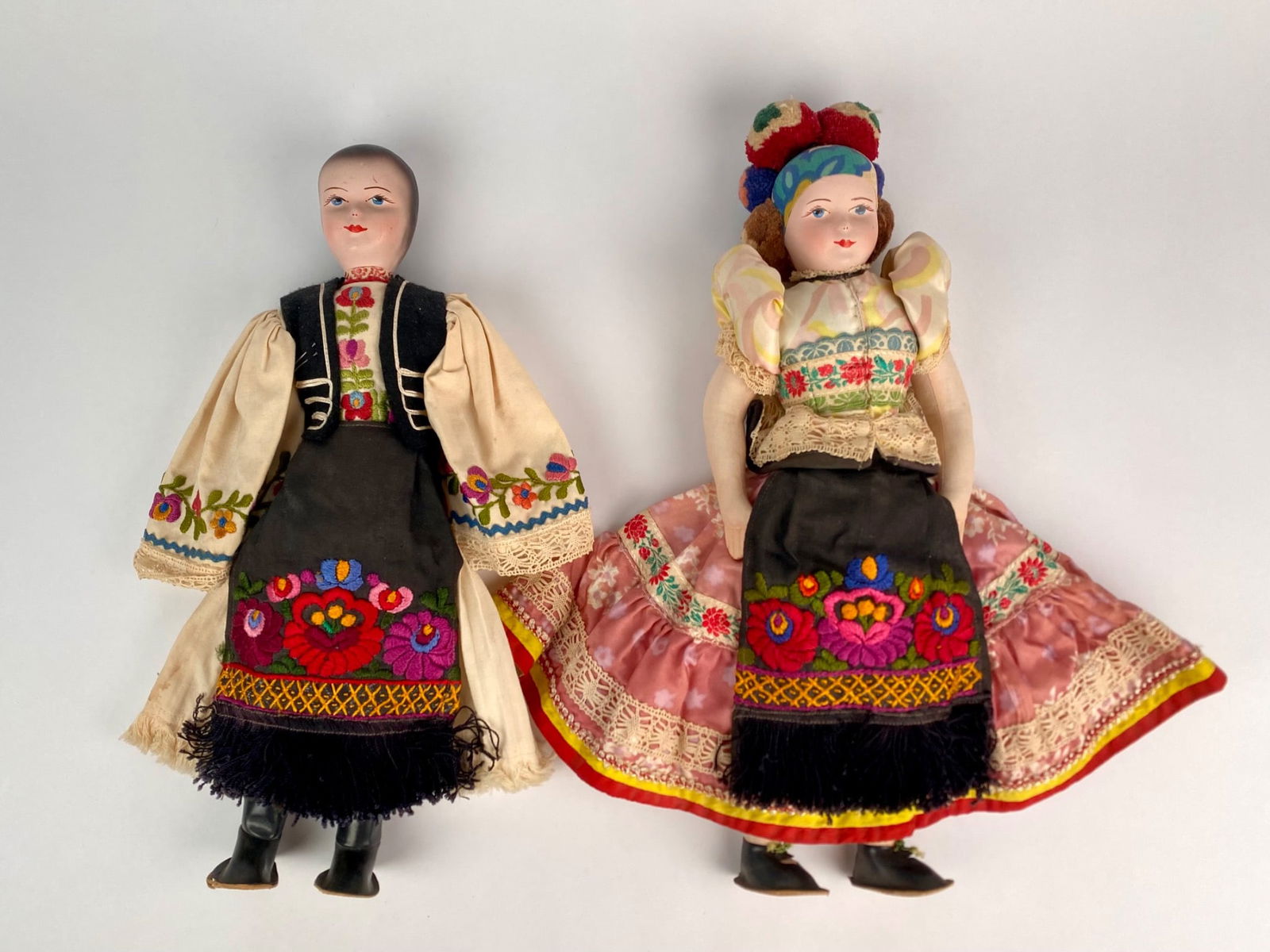 Pair of Vintage Hungarian Folk Art Dolls in Hand Embroidered Regional Dress: Pair of vintage Hungarian folk art dolls, each dressed in traditional regional attire. The female doll features a hand painted face, stuffed cloth body, and an ensemble with puffed sleeves, a lace tri