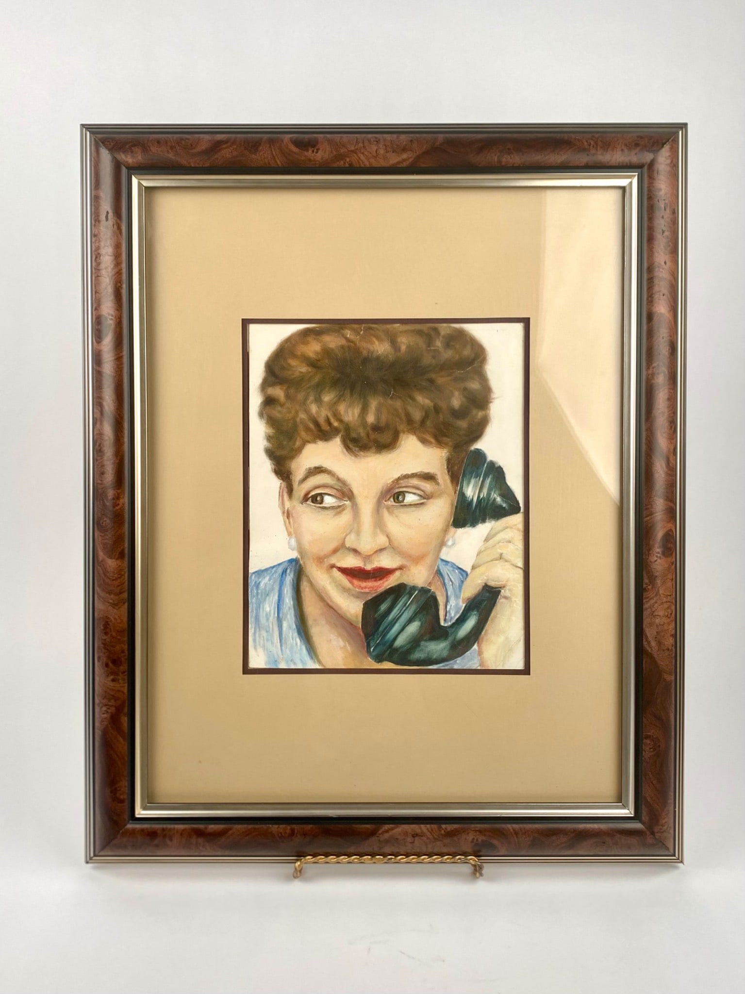 Framed Portrait Painting of a Woman on a Telephone: Framed painting of a woman depicted holding a black telephone handset, mounted on beige matting and enclosed in a wooden frame with a burled wood-style finish and metallic trim. The frame shows some w