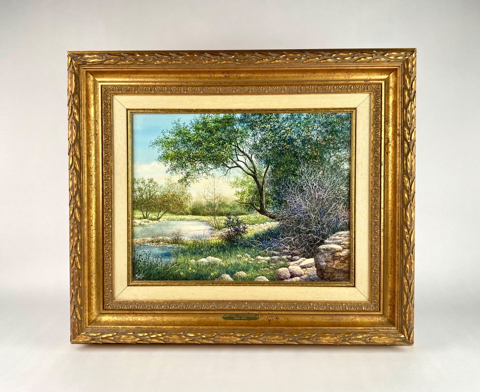 ‘April Solitude’ Oil on Canvas by Mostyn in Ornate Gilt Frame: Oil painting titled ‘April Solitude’ by artist Michael Mostyn, depicting a tranquil natural scene featuring a tree, water, and lush greenery. Signed by the artist on the lower left. Housed in an o