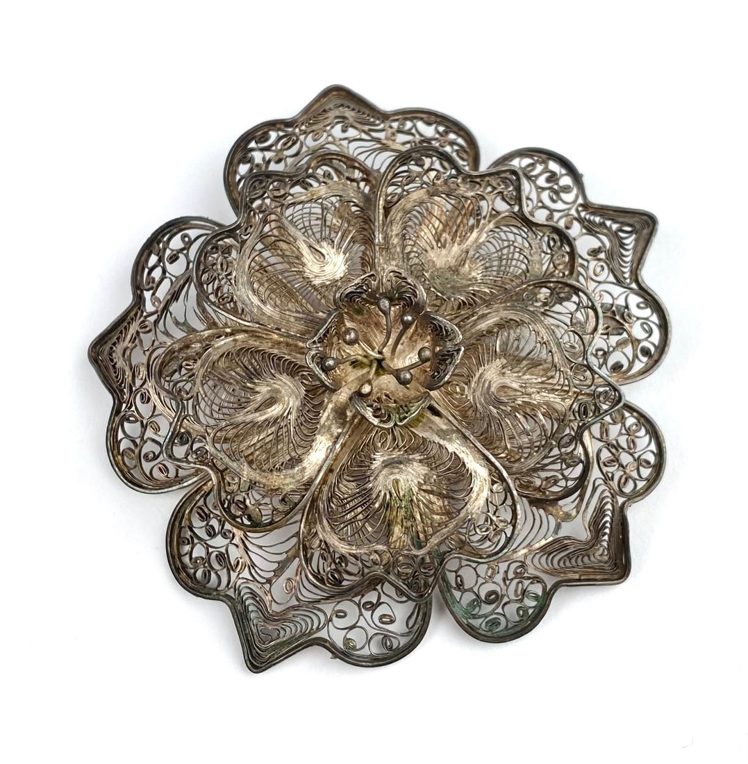 Vintage Sterling Silver Filigree Flower Brooch: Sterling silver brooch featuring an intricate filigree floral design. Marked ‘STERLING’ on the back. The brooch is equipped with a functional pin clasp. The brooch has patina consistent with age a